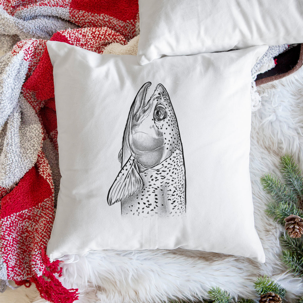White pillow cover printed with a detailed black ink illustration of a rainbow trout's head pointing upward, showing its spotted scales, on a woven chair.