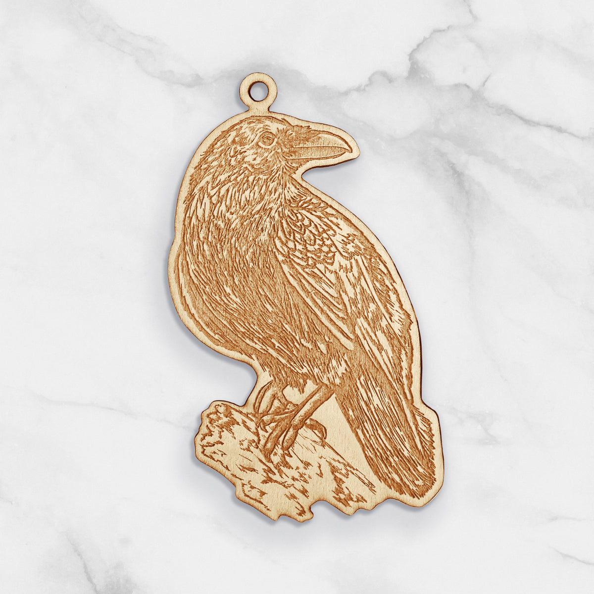 Wooden ornament featuring a detailed engraving of a raven perched, on a marble surface.