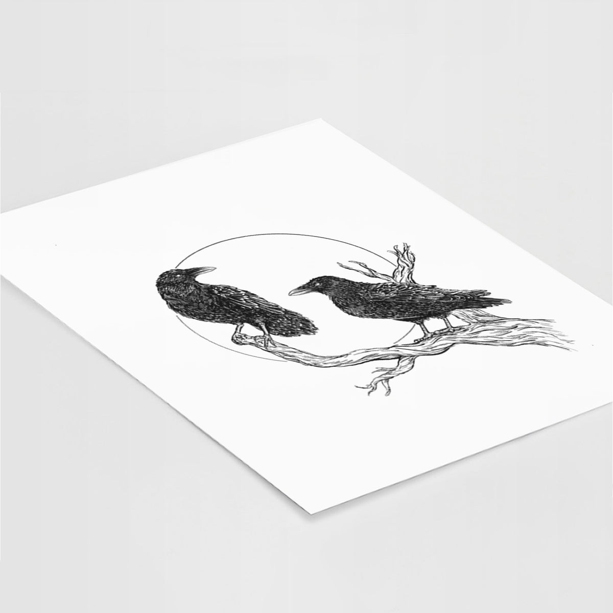 Art print of a black ink illustration of two ravens perched on a branch in front of a full moon, lying at an angle on a white surface.