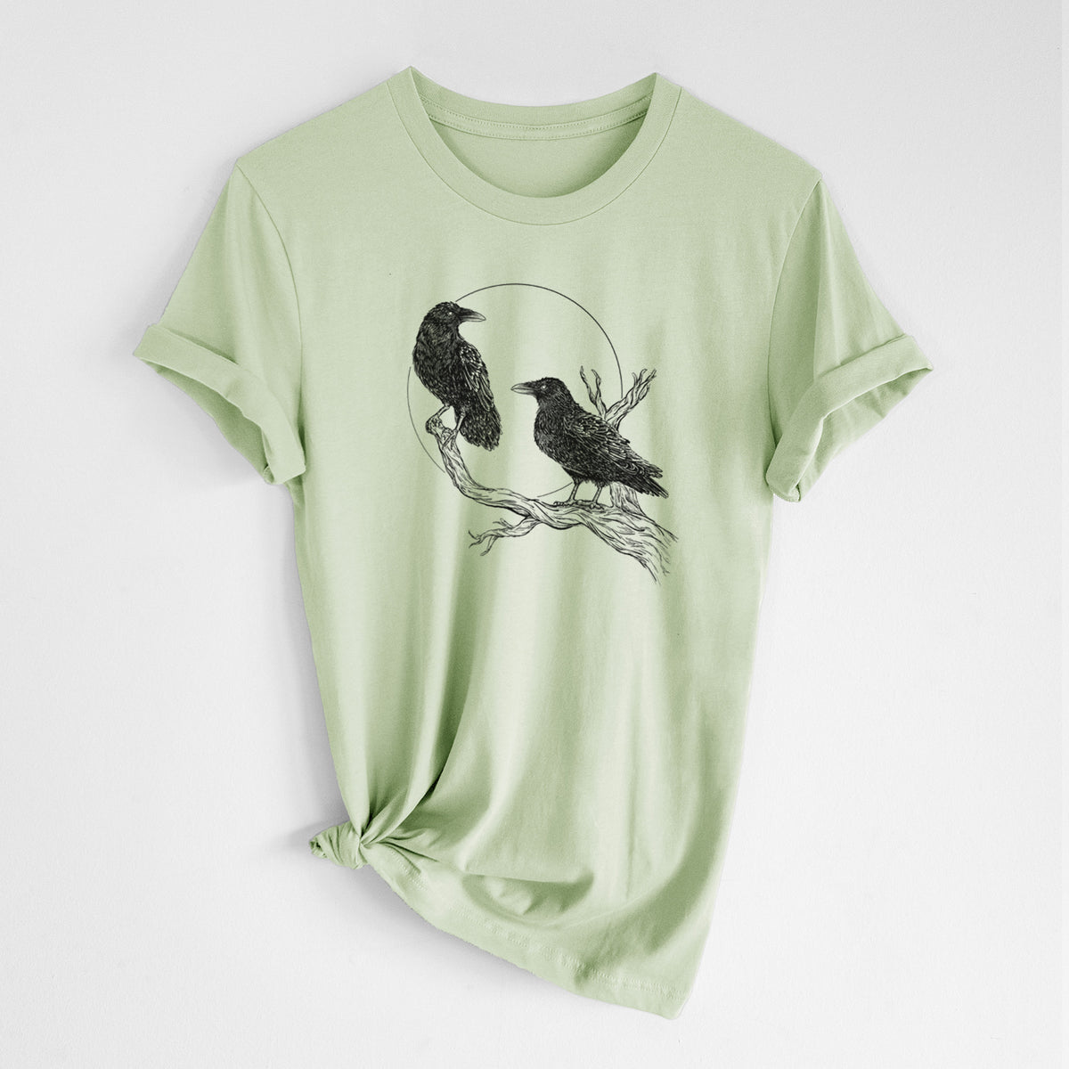 Spring green lightweight cotton t-shirt laid flat with the sleeves rolled, printed with a black ink illustration of two ravens perched on a branch in front of a full moon.
