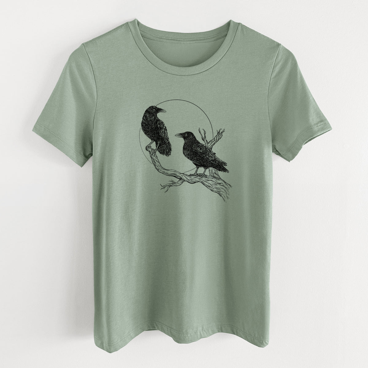 Sage green women's relaxed fit cotton t-shirt laid flat, printed with a black ink illustration of two ravens perched on a branch in front of a full moon.