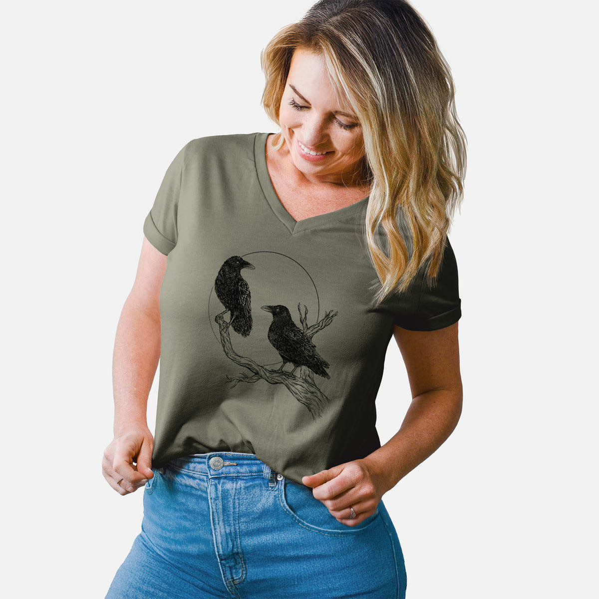 Woman wearing a military green women's relaxed fit cotton V-neck t-shirt printed with a black ink illustration of two ravens perched on a branch in front of a full moon.