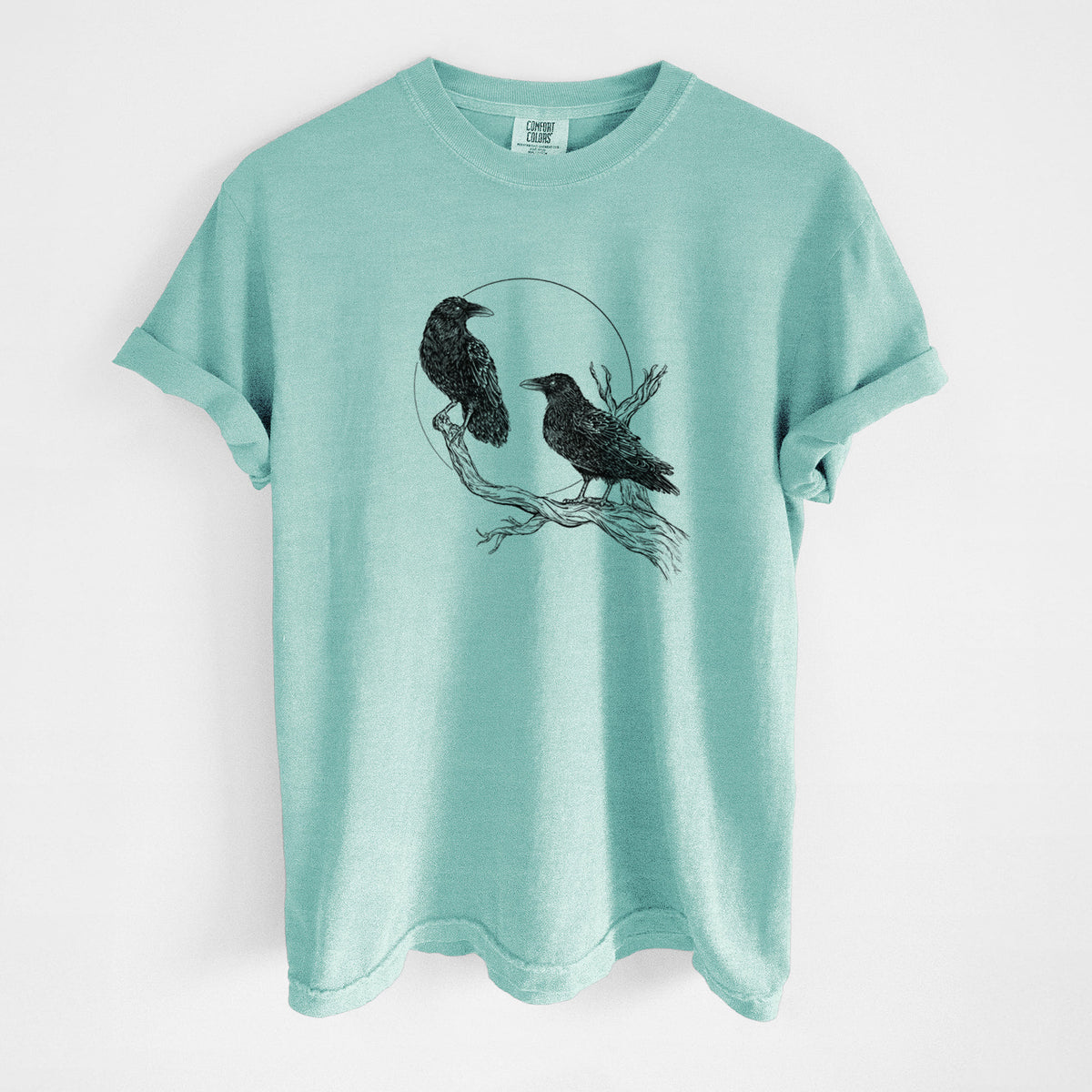 Chalky mint Comfort Colors t-shirt laid flat, printed with a black ink illustration of two ravens perched on a branch in front of a full moon.