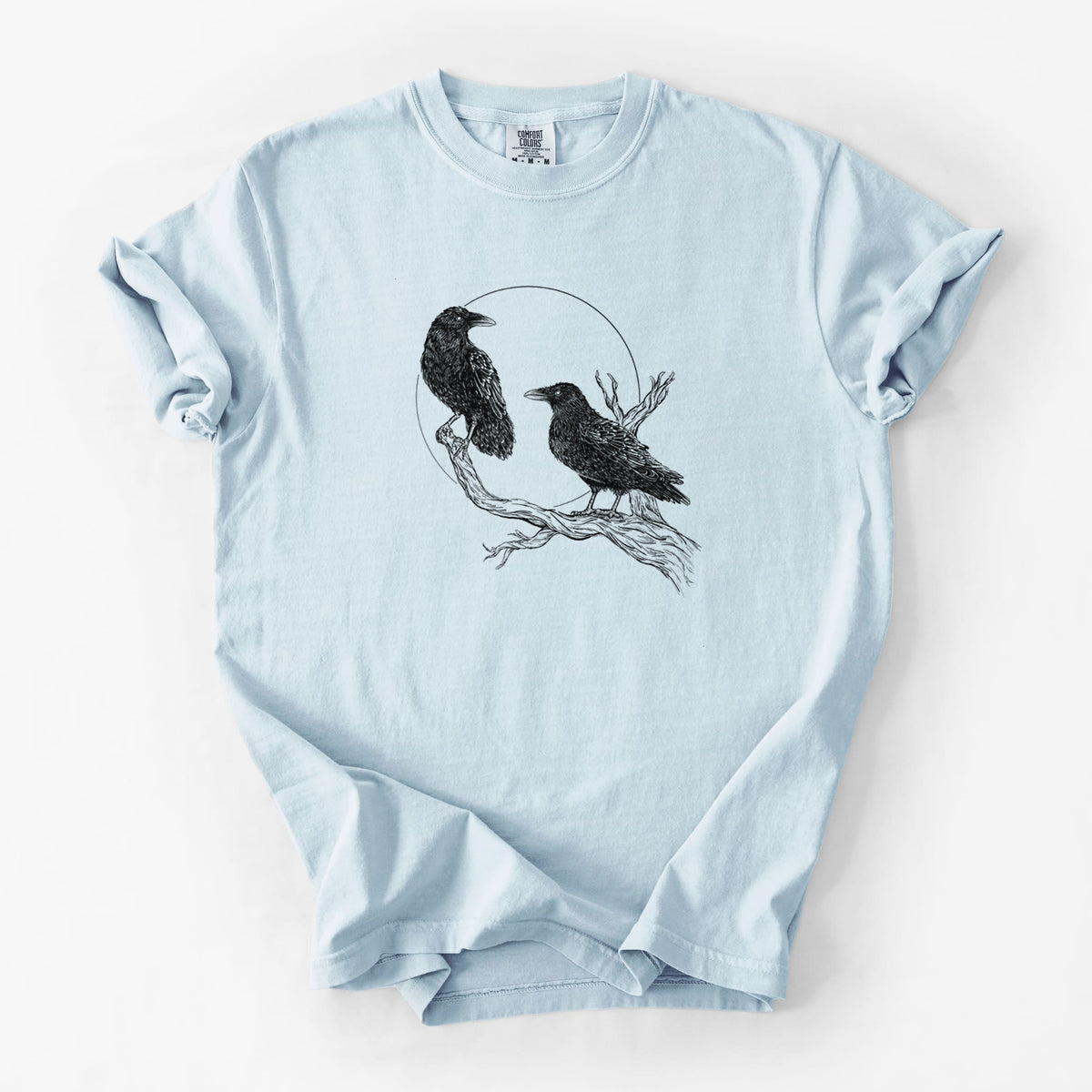 Chambray blue Comfort Colors t-shirt laid flat, printed with a black ink illustration of two ravens perched on a branch in front of a full moon.