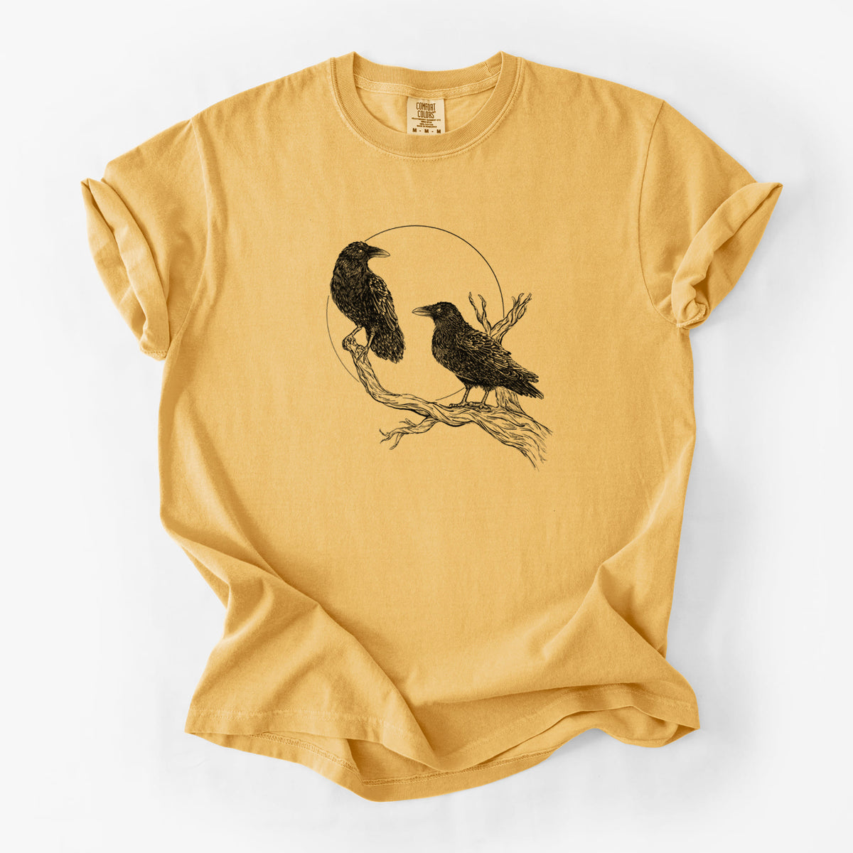 Golden wheat yellow Comfort Colors t-shirt laid flat, printed with a black ink illustration of two ravens perched on a branch in front of a full moon.