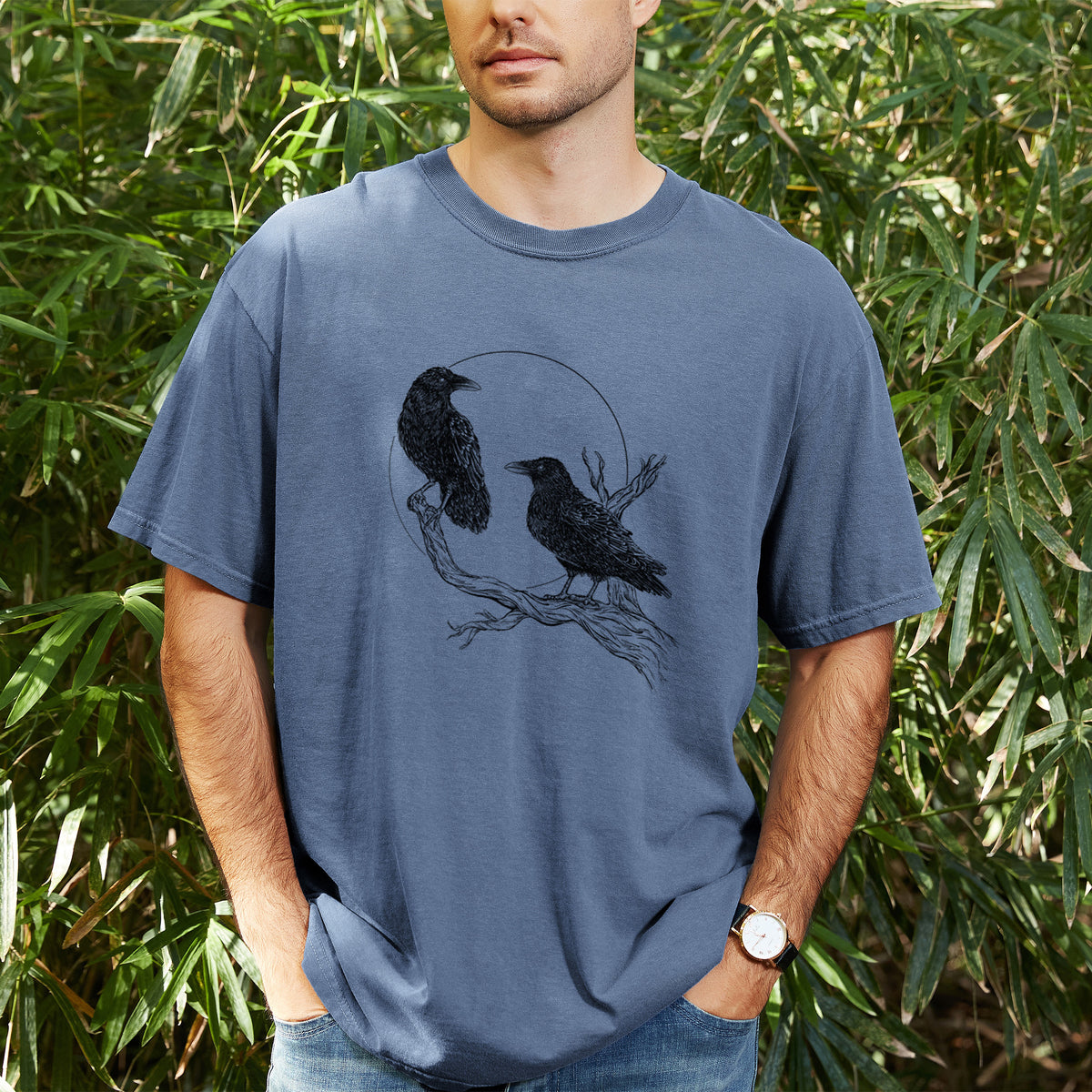 Man wearing a Comfort Colors t-shirt printed with a black ink illustration of two ravens perched on a branch in front of a full moon, outdoors.