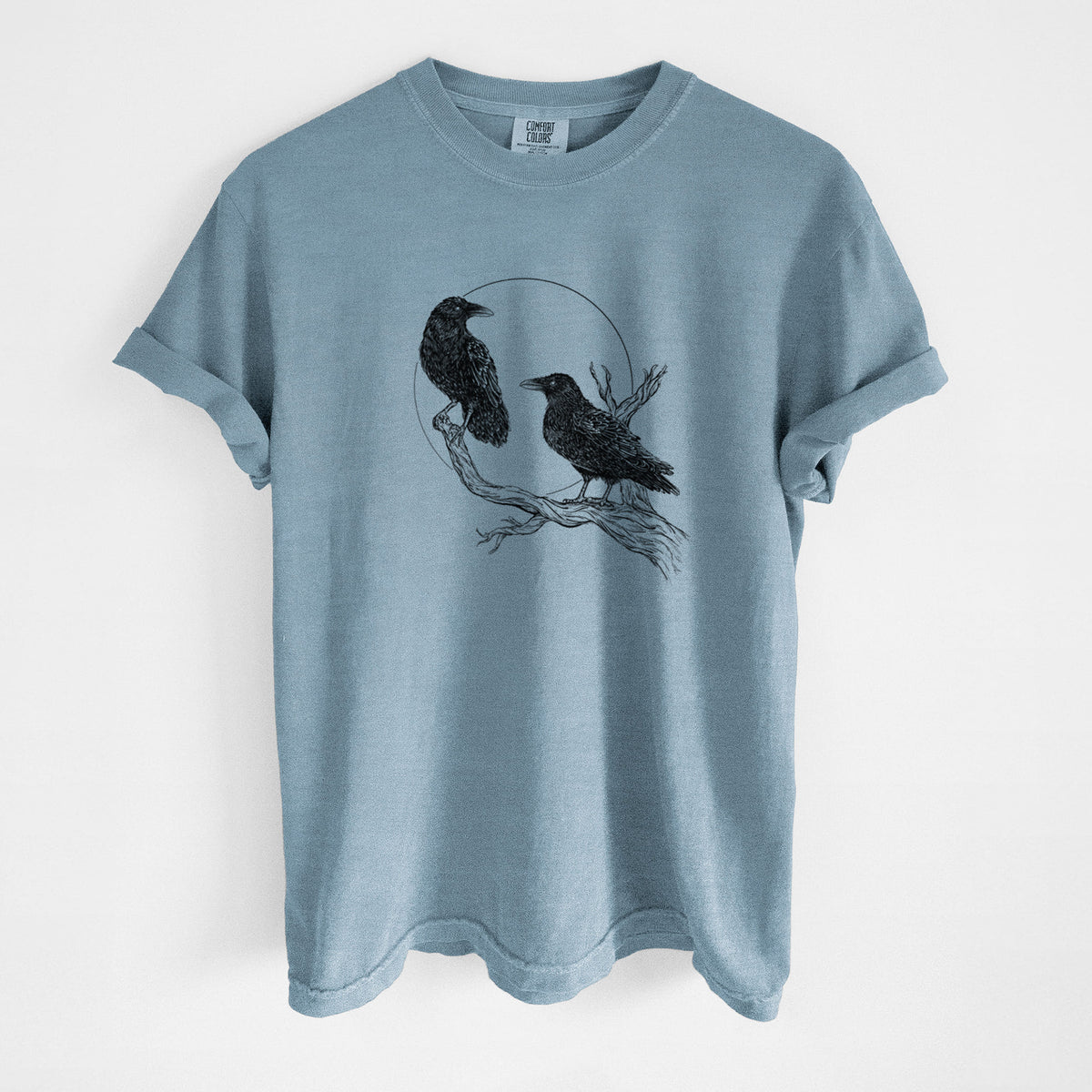 Steel blue Comfort Colors t-shirt laid flat, printed with a black ink illustration of two ravens perched on a branch in front of a full moon.