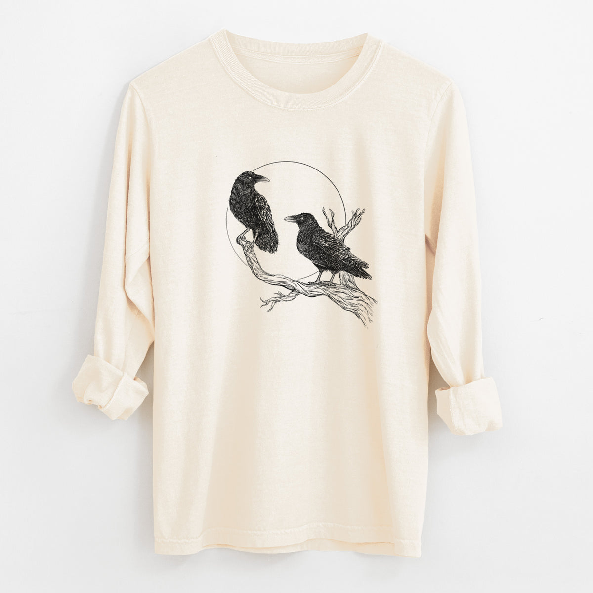 Ivory Comfort Colors long sleeve shirt laid flat with the cuffs rolled, printed with a black ink illustration of two ravens perched on a branch in front of a full moon.