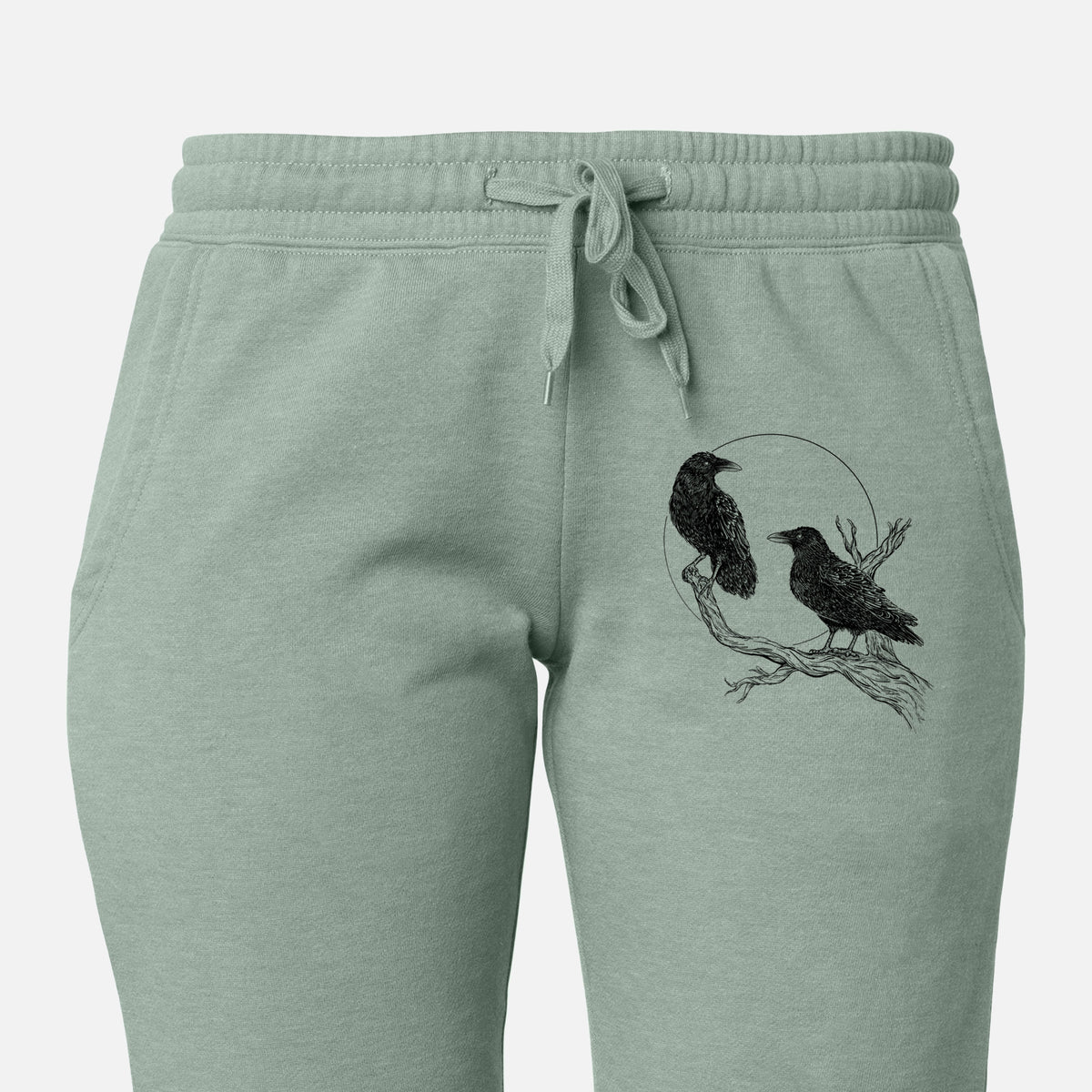 Front of sage green Cali Wave sweatpants, printed with a black ink illustration of two ravens perched on a branch in front of a full moon on the leg.