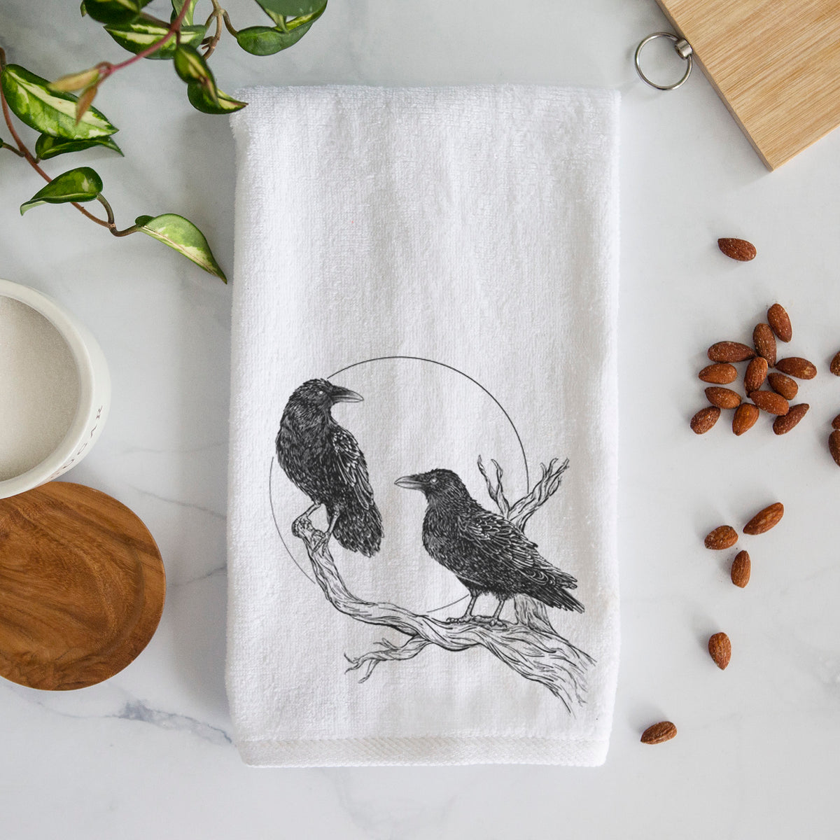White hand towel printed with a black ink illustration of two ravens perched on a branch in front of a full moon.