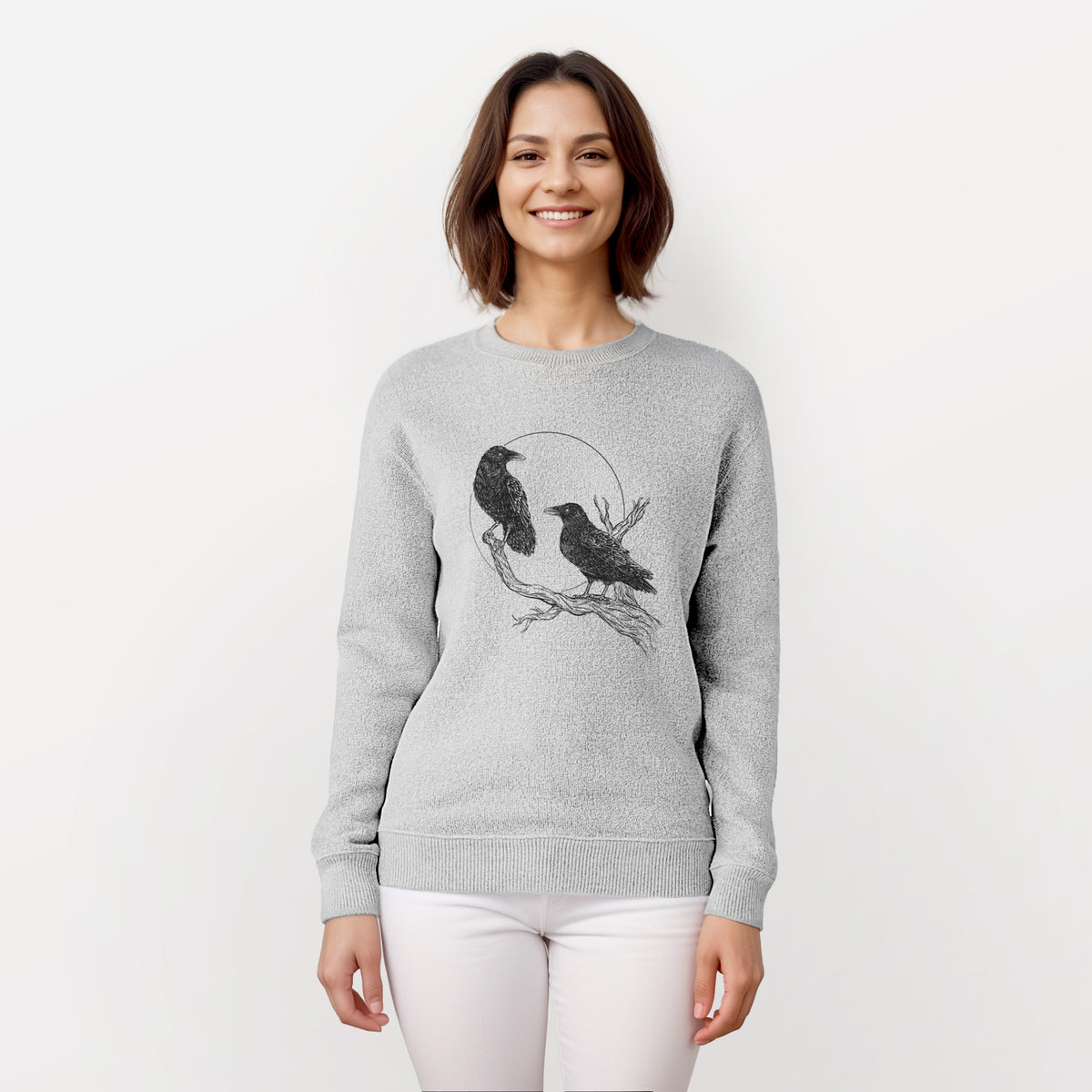 Woman wearing a knit sweatshirt printed with a black ink illustration of two ravens perched on a branch in front of a full moon.