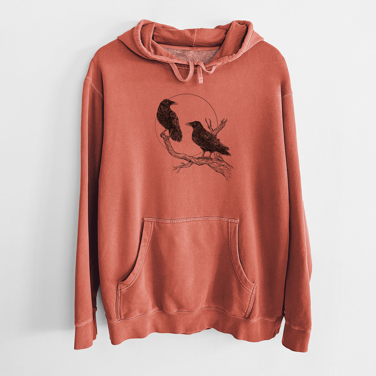 Amber orange pigment dyed hoodie laid flat, printed with a black ink illustration of two ravens perched on a branch in front of a full moon.
