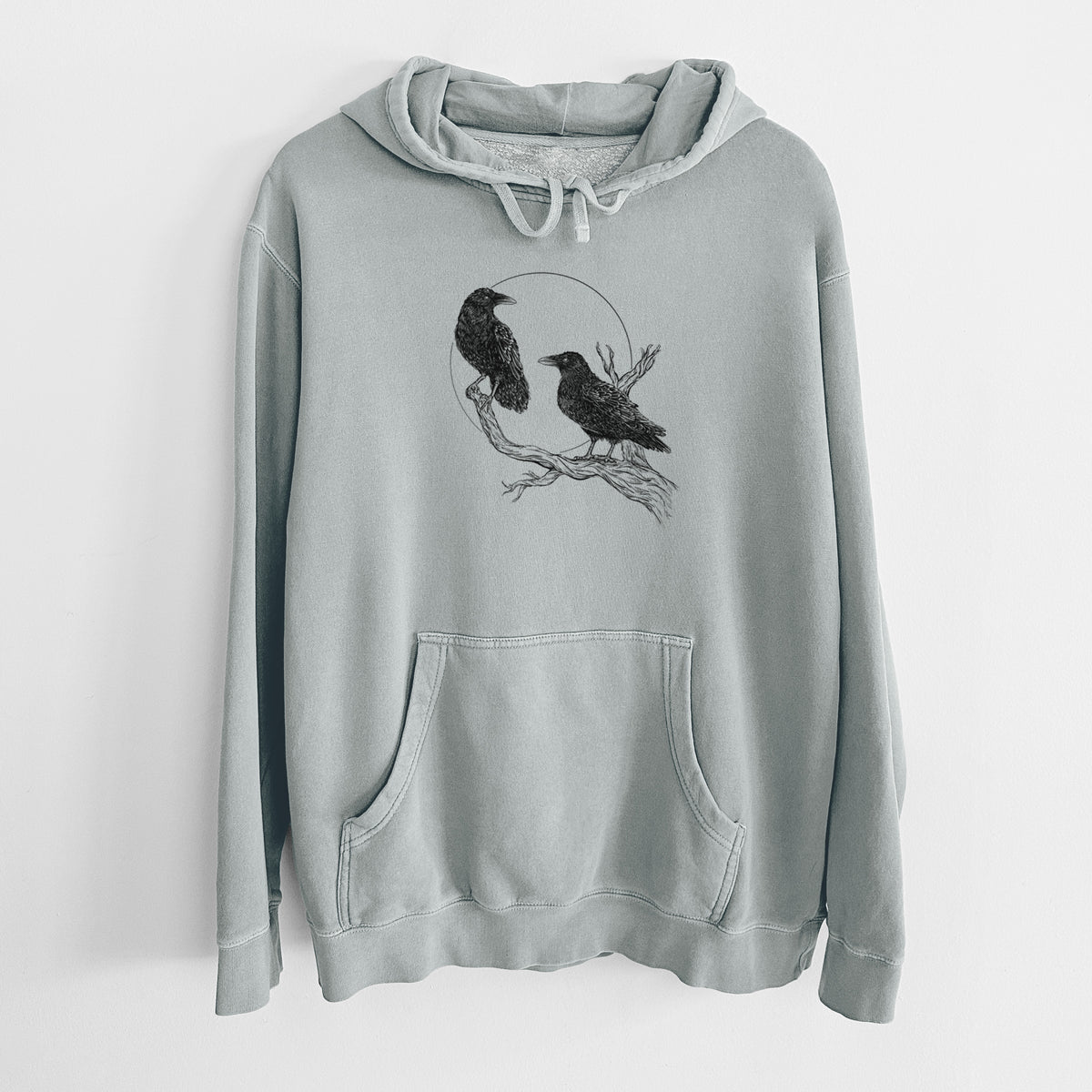 Sage green pigment dyed hoodie laid flat, printed with a black ink illustration of two ravens perched on a branch in front of a full moon.