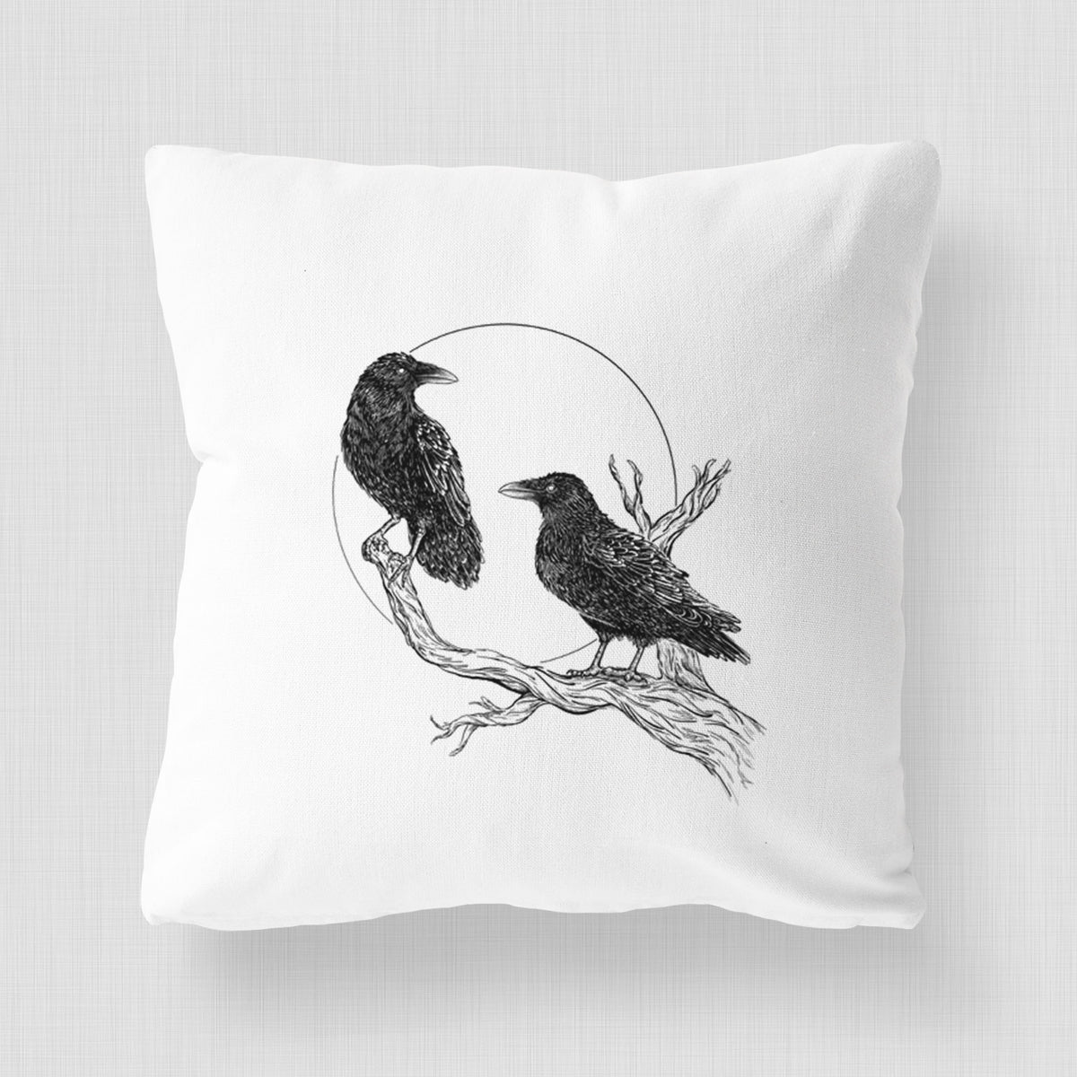 White pillow cover printed with a black ink illustration of two ravens perched on a branch in front of a full moon.