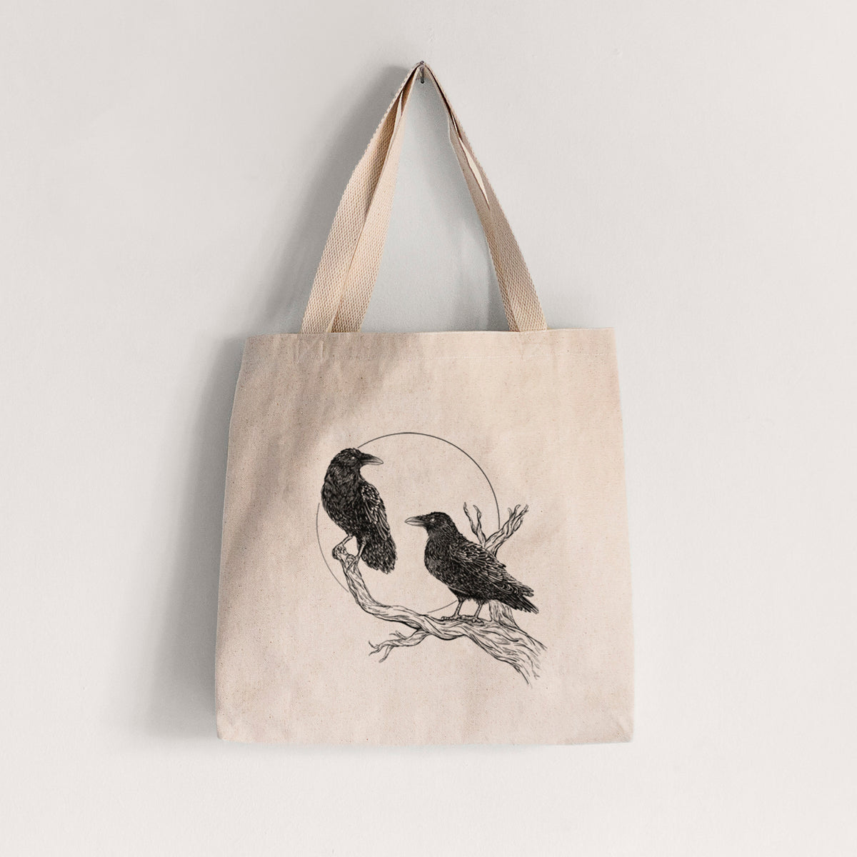 Natural canvas tote bag printed with a black ink illustration of two ravens perched on a branch in front of a full moon.