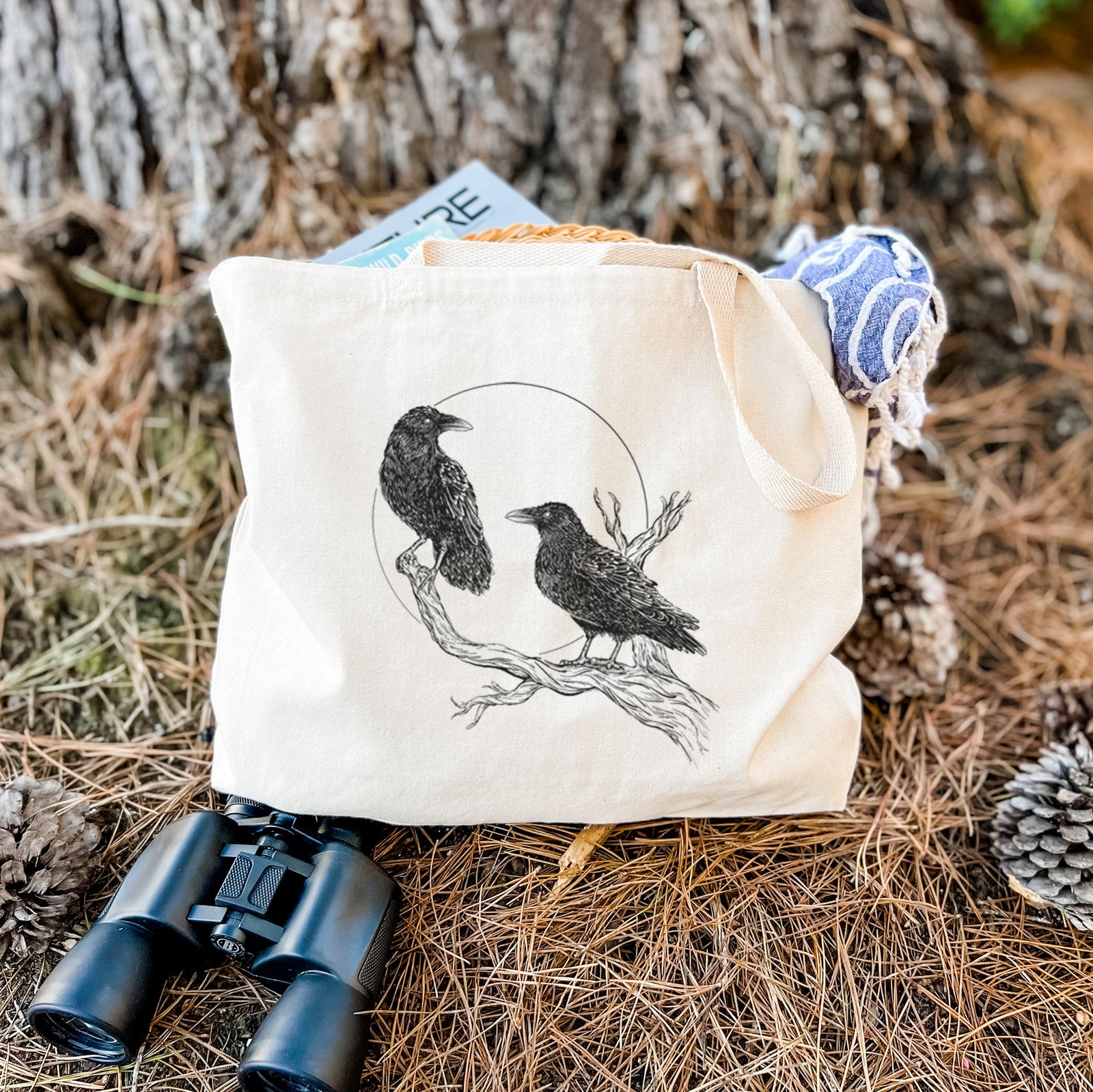Natural canvas tote bag printed with a black ink illustration of two ravens perched on a branch in front of a full moon.