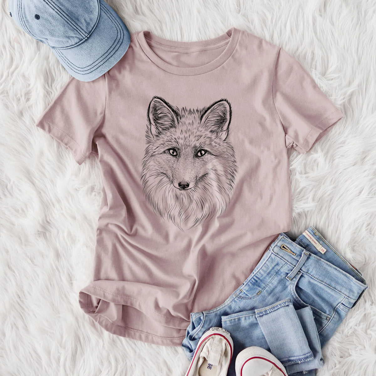 Women's relaxed fit cotton t-shirt printed with a detailed black ink sketch of a red fox's face looking straight ahead, its fur drawn in fine pencil-like strokes, styled flat on a white faux fur rug with jeans.