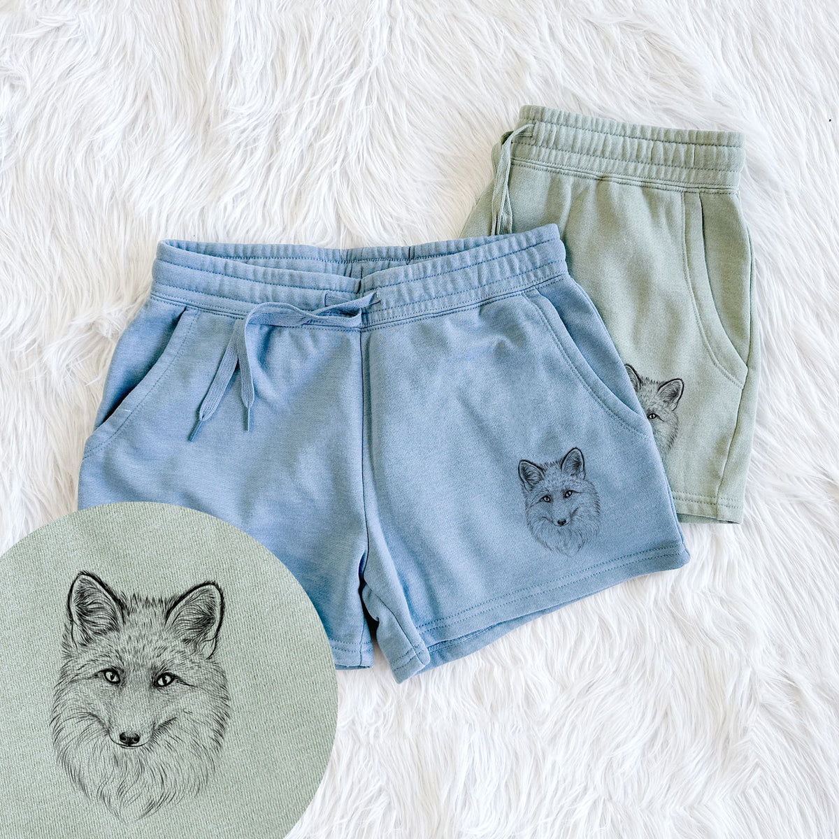 Two pairs of Cali Wave shorts in different colors printed with a detailed black ink sketch of a red fox's face looking straight ahead, its fur drawn in fine pencil-like strokes, with a close-up of the print.