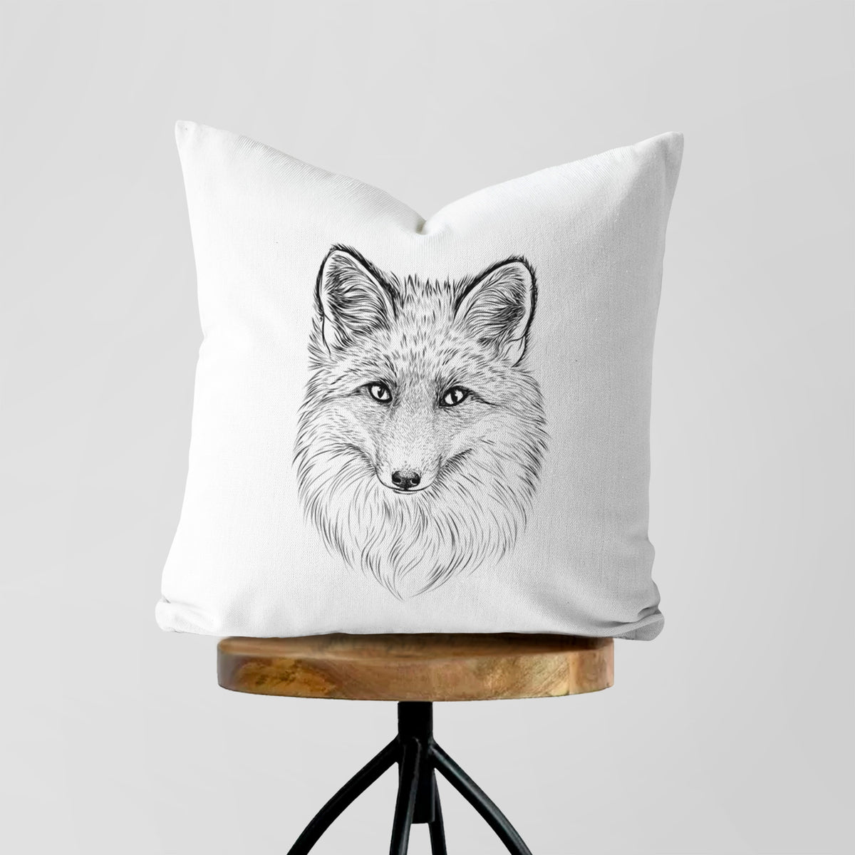 White pillow cover printed with a detailed black ink sketch of a red fox's face looking straight ahead, its fur drawn in fine pencil-like strokes, on a wooden stool.