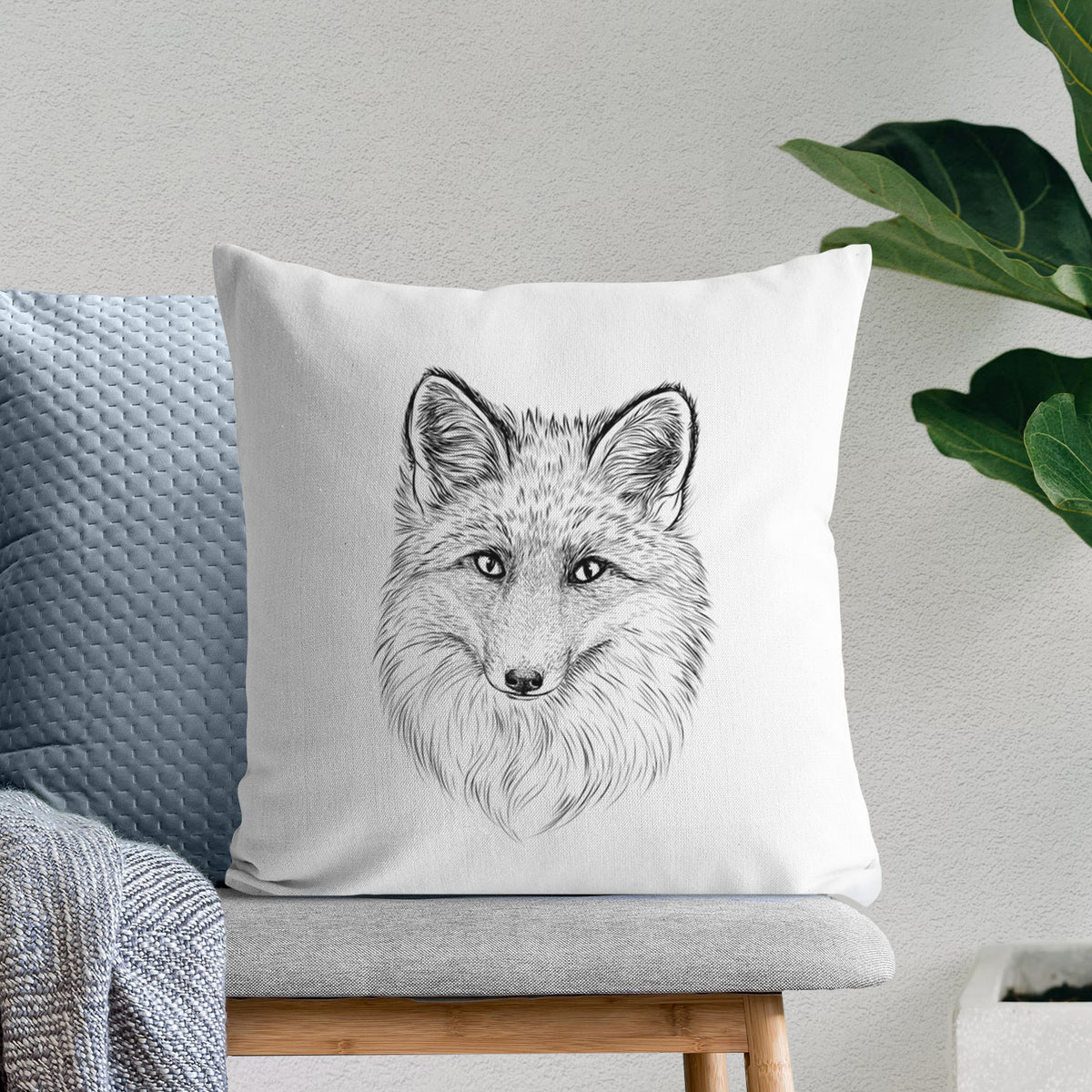 White pillow cover printed with a detailed black ink sketch of a red fox's face looking straight ahead, its fur drawn in fine pencil-like strokes, on a bench beside plants.