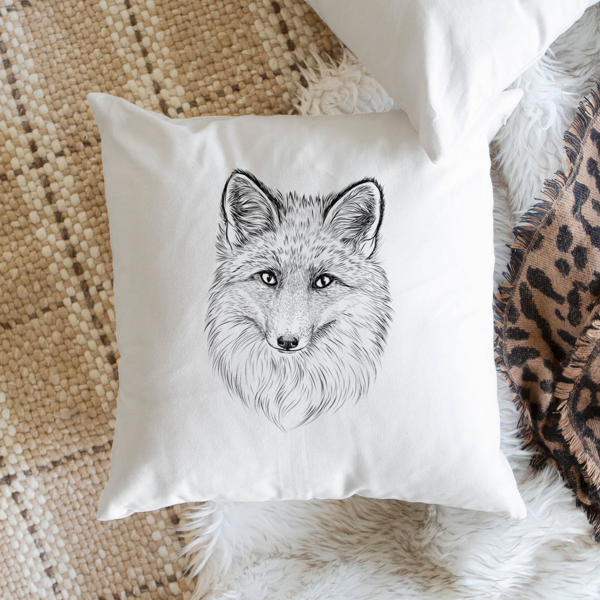 White pillow cover printed with a detailed black ink sketch of a red fox's face looking straight ahead, its fur drawn in fine pencil-like strokes, on a woven chair.