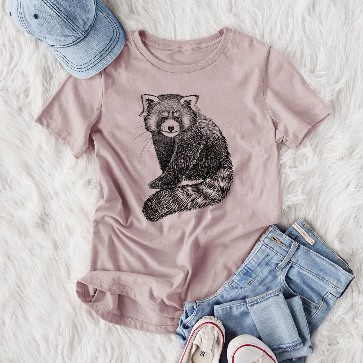 Women's relaxed fit cotton t-shirt printed with a detailed black ink illustration of a red panda sitting with its striped tail wrapped around, styled flat on a white faux fur rug with jeans.