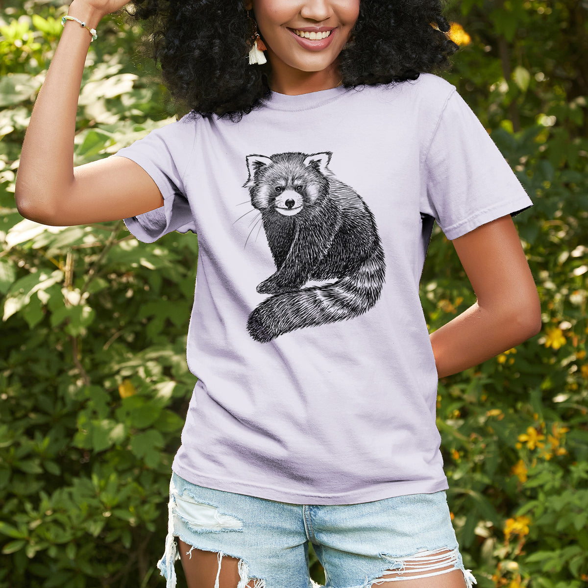 Woman wearing a Comfort Colors t-shirt printed with a detailed black ink illustration of a red panda sitting with its striped tail wrapped around, outdoors.