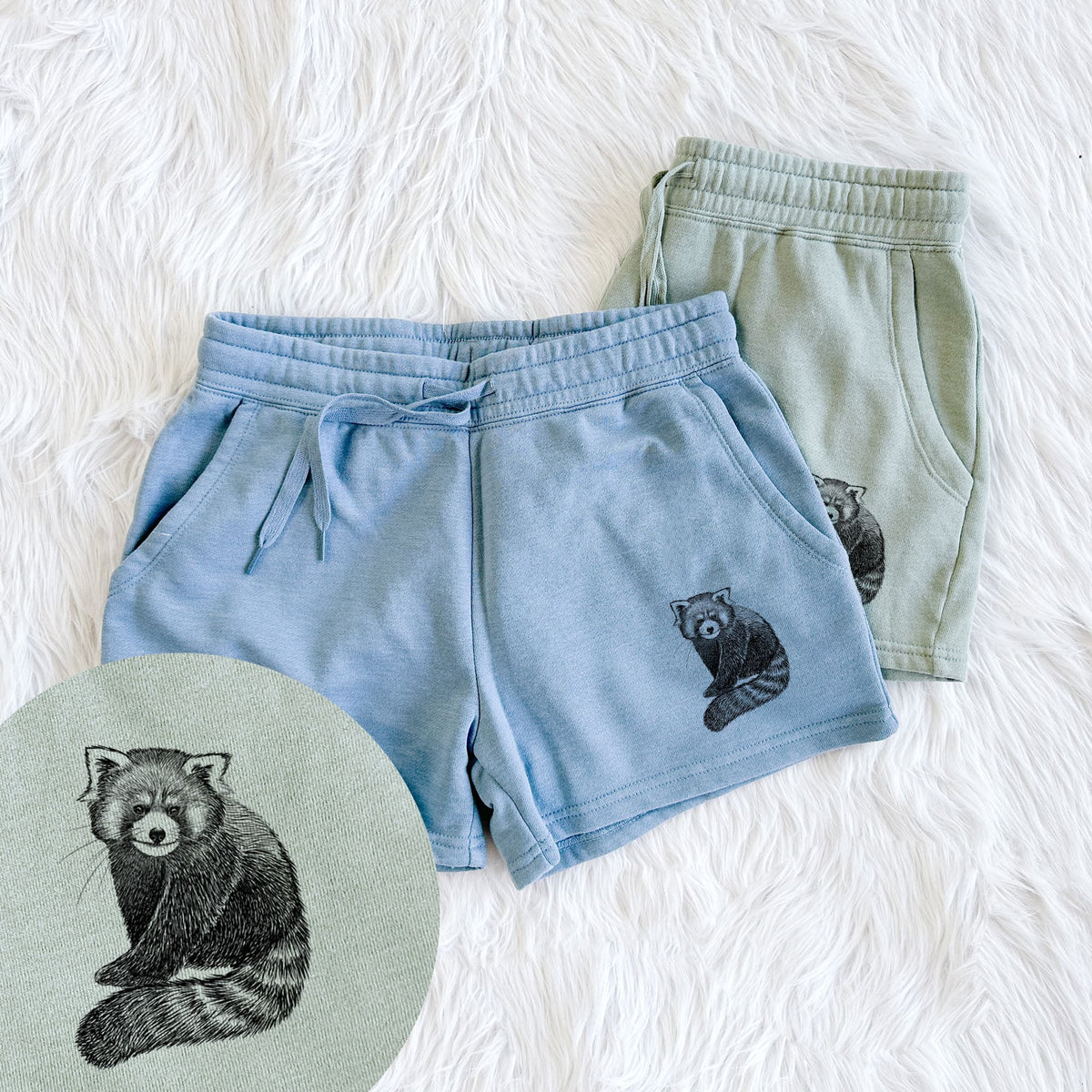 Two pairs of Cali Wave shorts in different colors printed with a detailed black ink illustration of a red panda sitting with its striped tail wrapped around, with a close-up of the print.