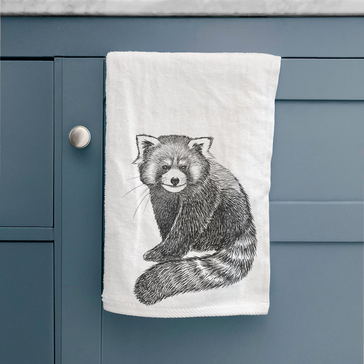 White hand towel printed with a detailed black ink illustration of a red panda sitting with its striped tail wrapped around, hanging on a cabinet door.