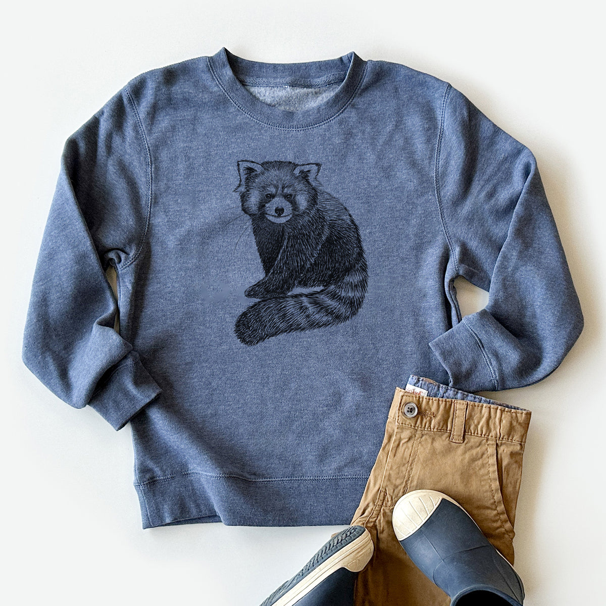 Youth crewneck sweatshirt printed with a detailed black ink illustration of a red panda sitting with its striped tail wrapped around, styled flat with khaki pants and shoes.
