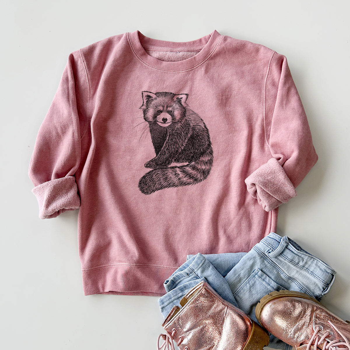 Youth crewneck sweatshirt printed with a detailed black ink illustration of a red panda sitting with its striped tail wrapped around, styled flat with jeans and boots.