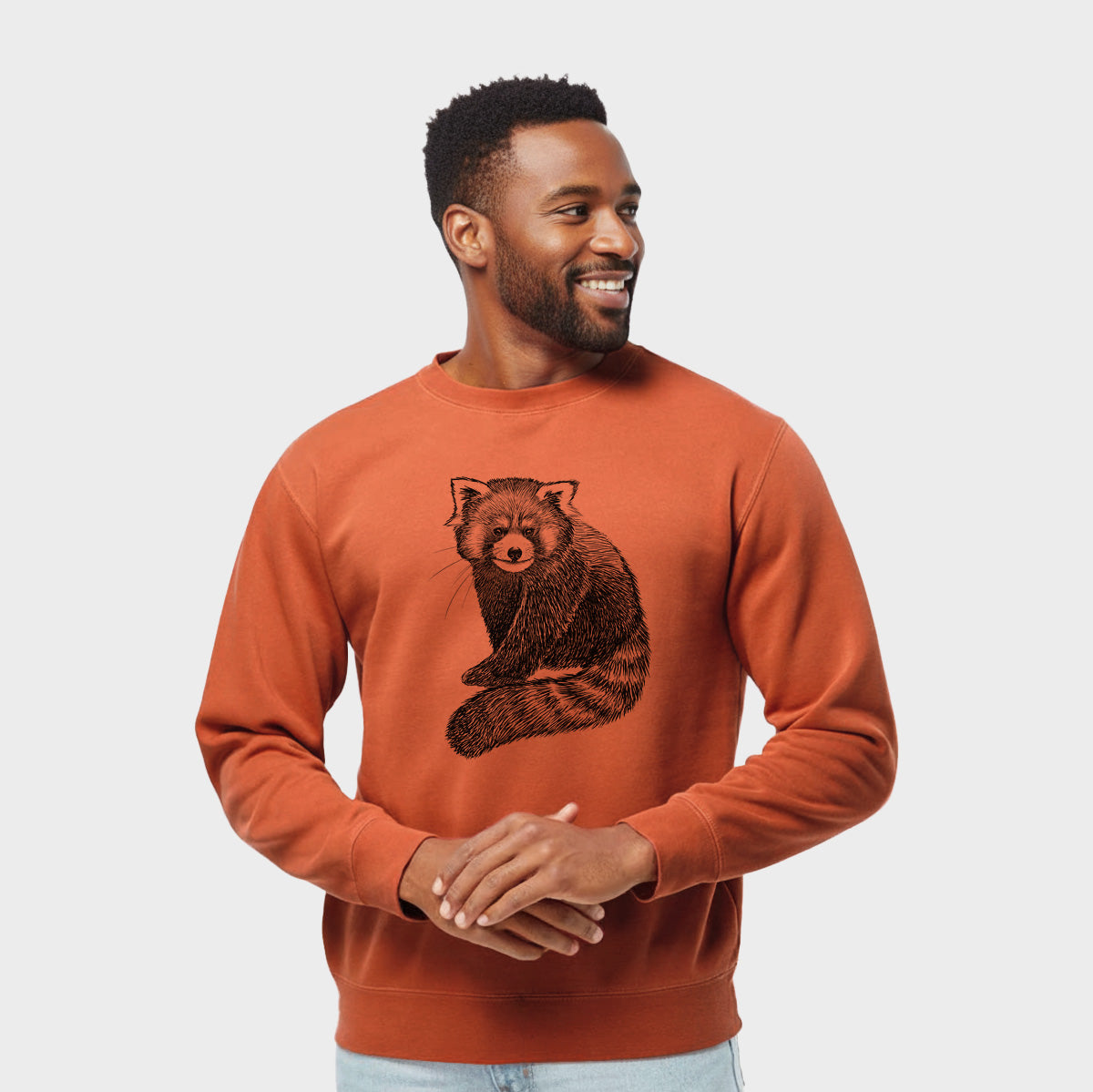 Model wearing an amber orange pigment dyed crewneck sweatshirt printed with a detailed black ink illustration of a red panda sitting with its striped tail wrapped around.
