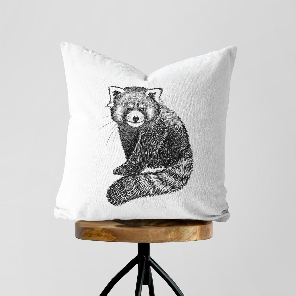 White pillow cover printed with a detailed black ink illustration of a red panda sitting with its striped tail wrapped around, on a wooden stool.
