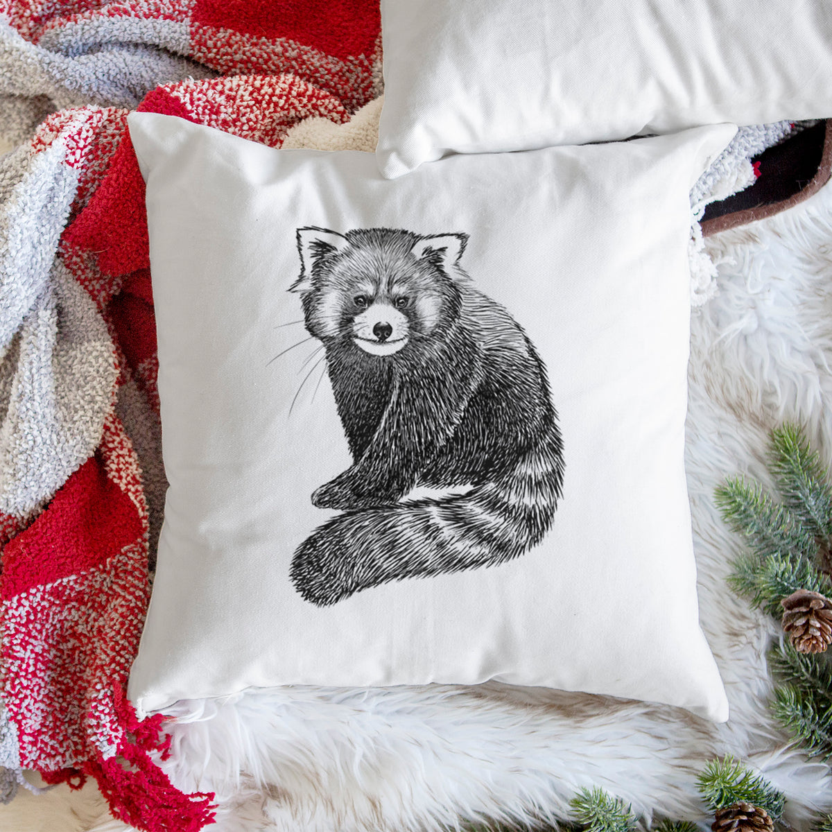 White pillow cover printed with a detailed black ink illustration of a red panda sitting with its striped tail wrapped around, on a woven chair.