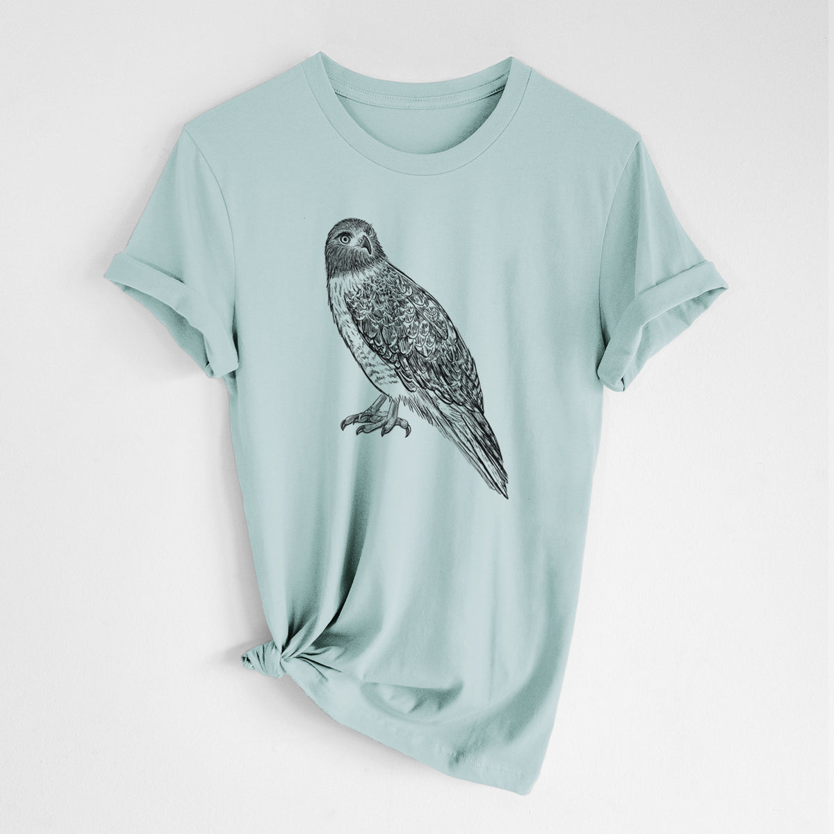 Dusty blue lightweight cotton t-shirt laid flat with the sleeves rolled, printed with a detailed black ink illustration of a red-tailed hawk perched.