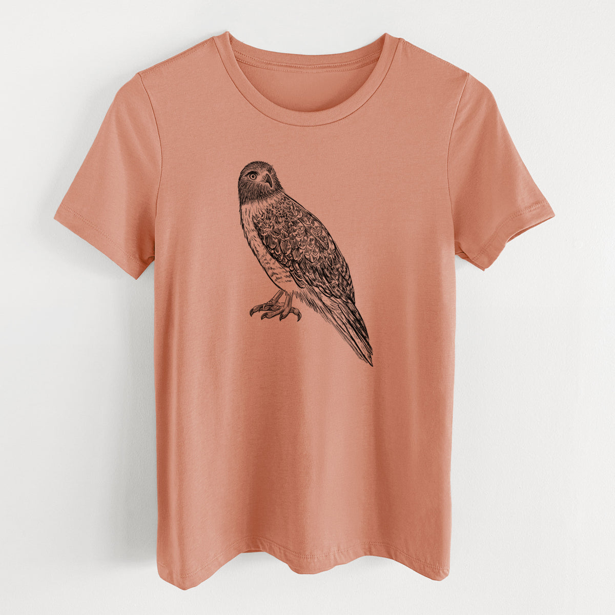 Terracotta orange women's relaxed fit cotton t-shirt laid flat, printed with a detailed black ink illustration of a red-tailed hawk perched.