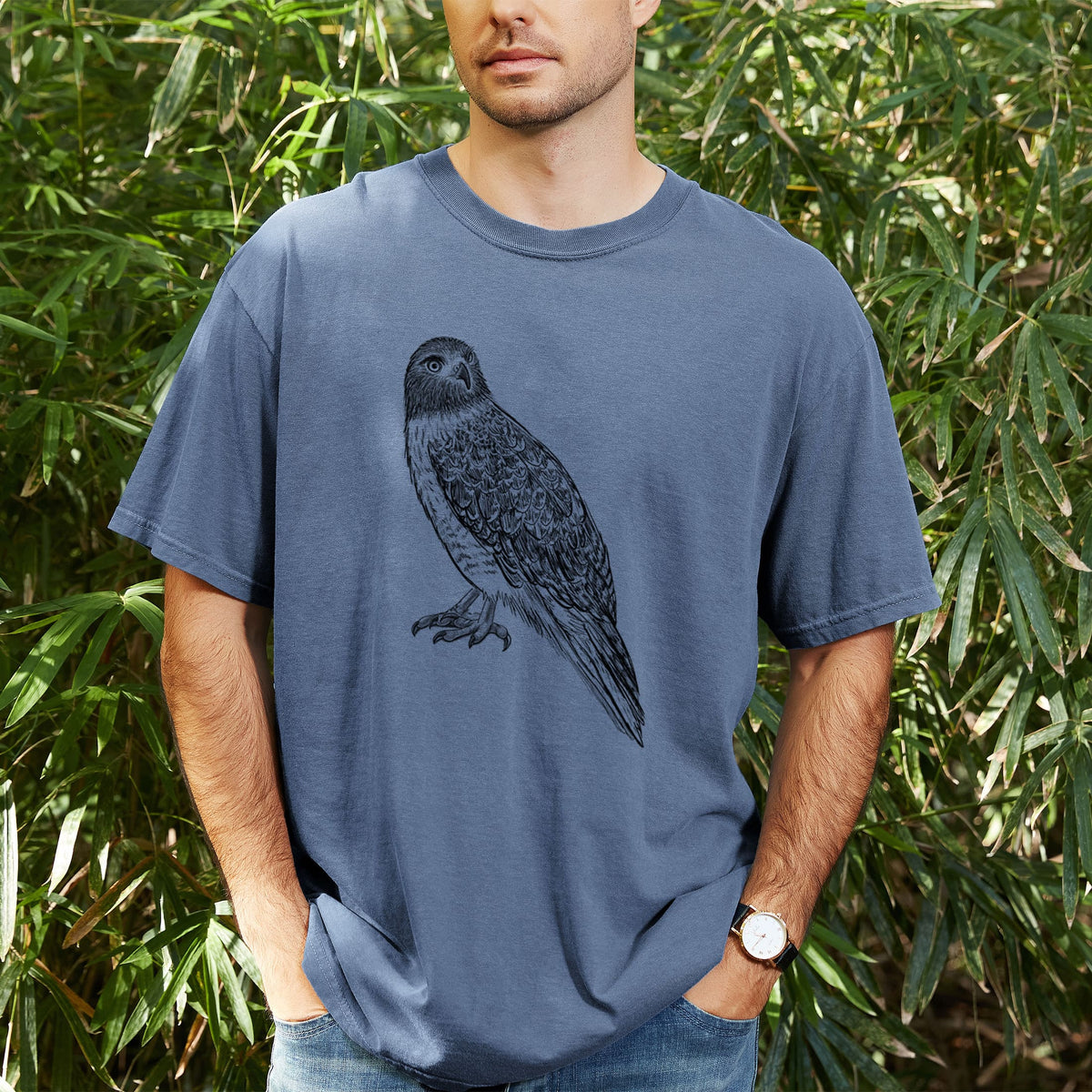 Man wearing a Comfort Colors t-shirt printed with a detailed black ink illustration of a red-tailed hawk perched, outdoors.