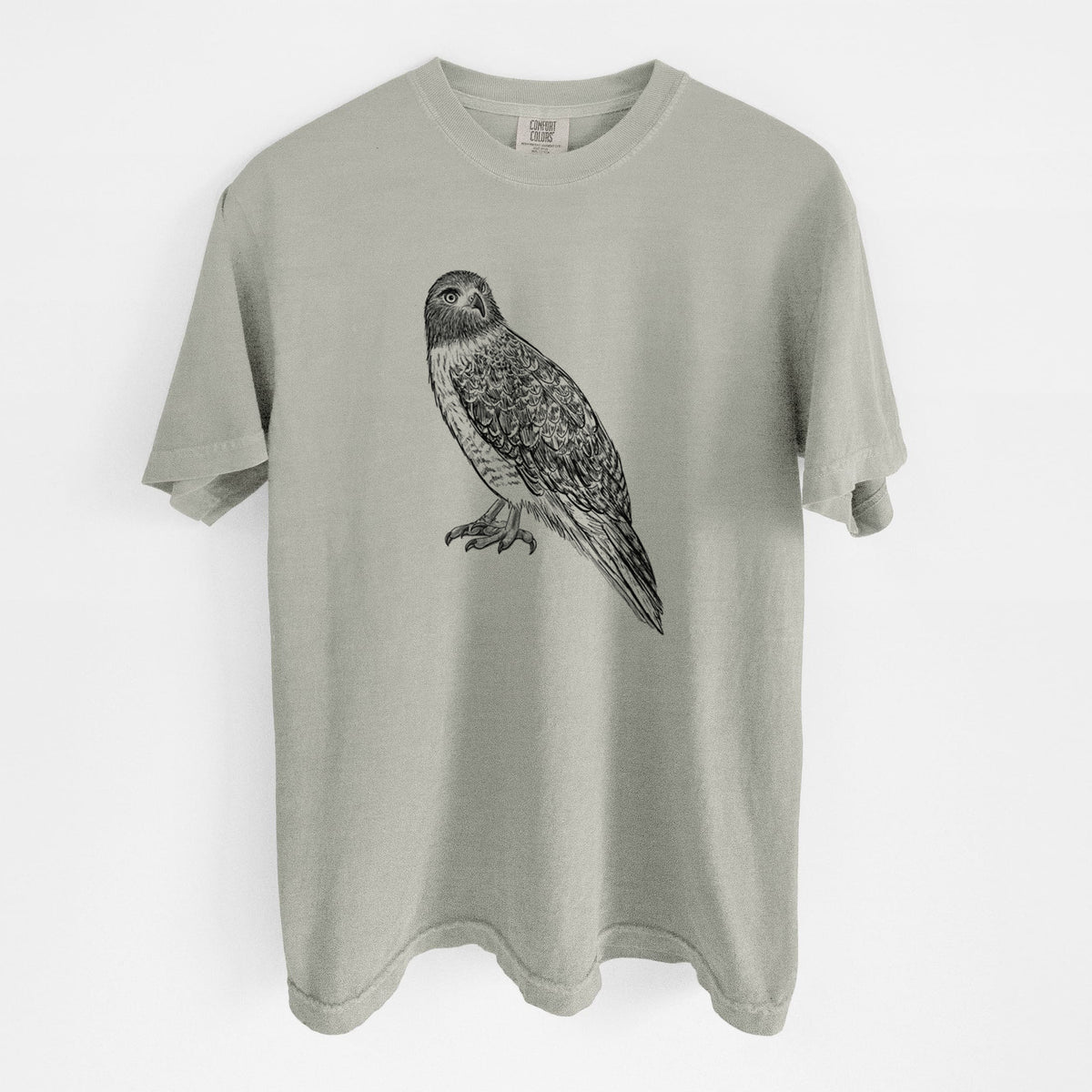 Sandstone beige Comfort Colors t-shirt laid flat, printed with a detailed black ink illustration of a red-tailed hawk perched.