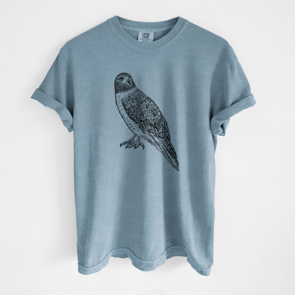 Steel blue Comfort Colors t-shirt laid flat, printed with a detailed black ink illustration of a red-tailed hawk perched.