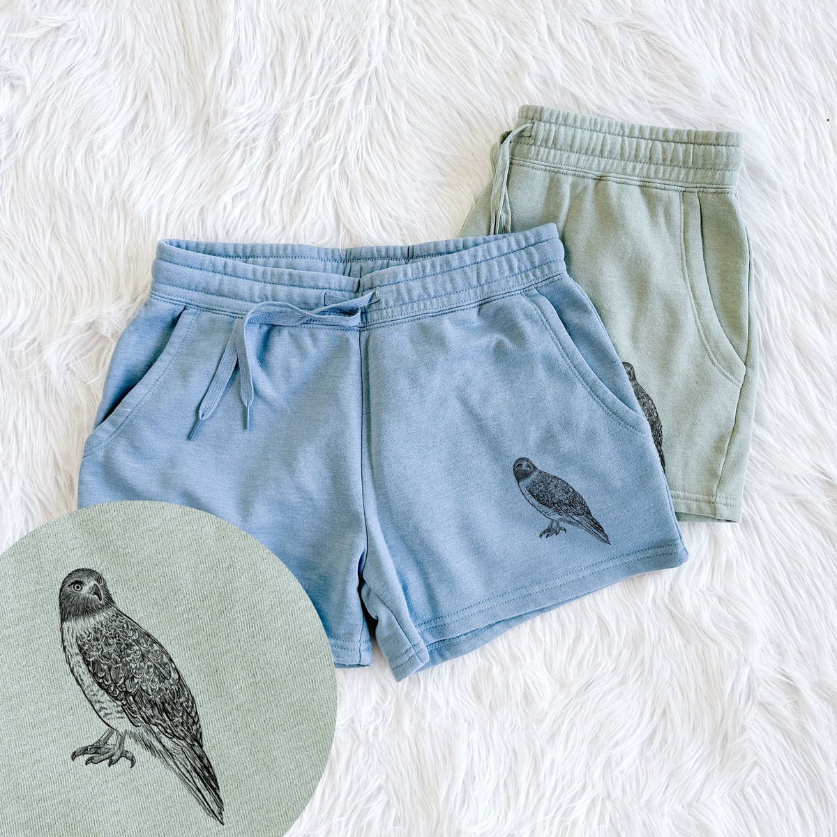 Two pairs of Cali Wave shorts in different colors printed with a detailed black ink illustration of a red-tailed hawk perched, with a close-up of the print.