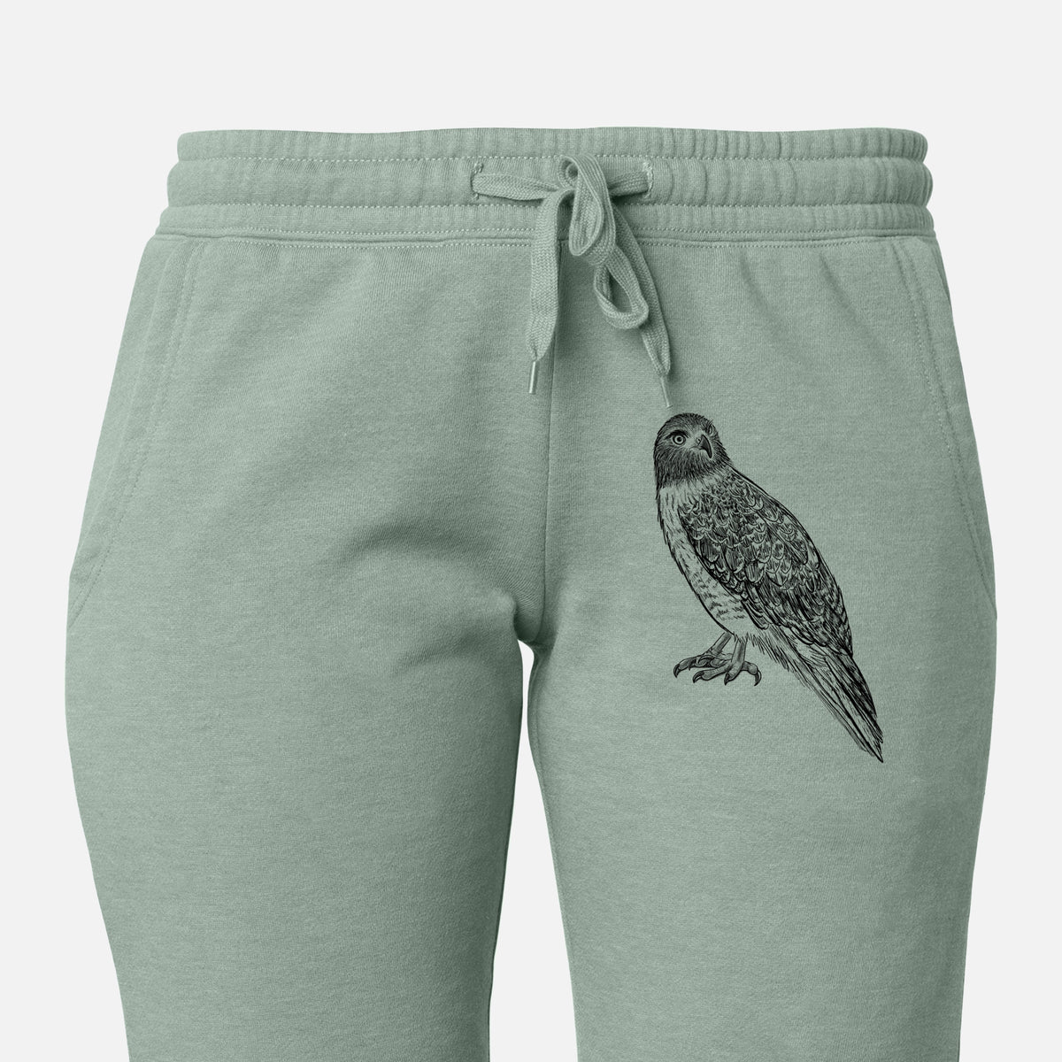 Front of sage green Cali Wave sweatpants, printed with a detailed black ink illustration of a red-tailed hawk perched on the leg.
