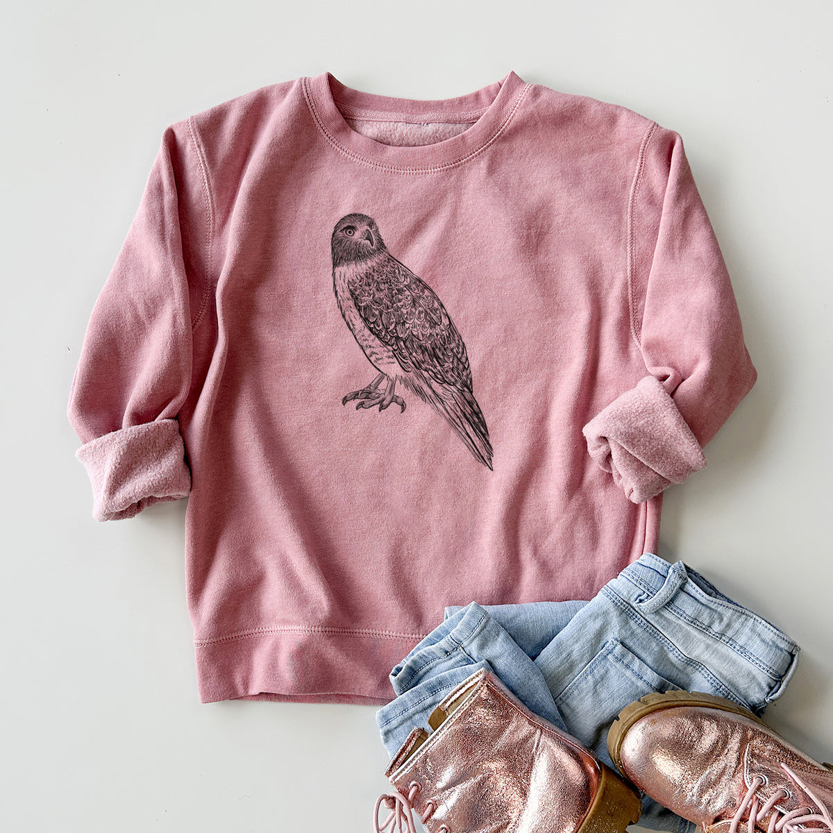 Youth crewneck sweatshirt printed with a detailed black ink illustration of a red-tailed hawk perched, styled flat with jeans and boots.