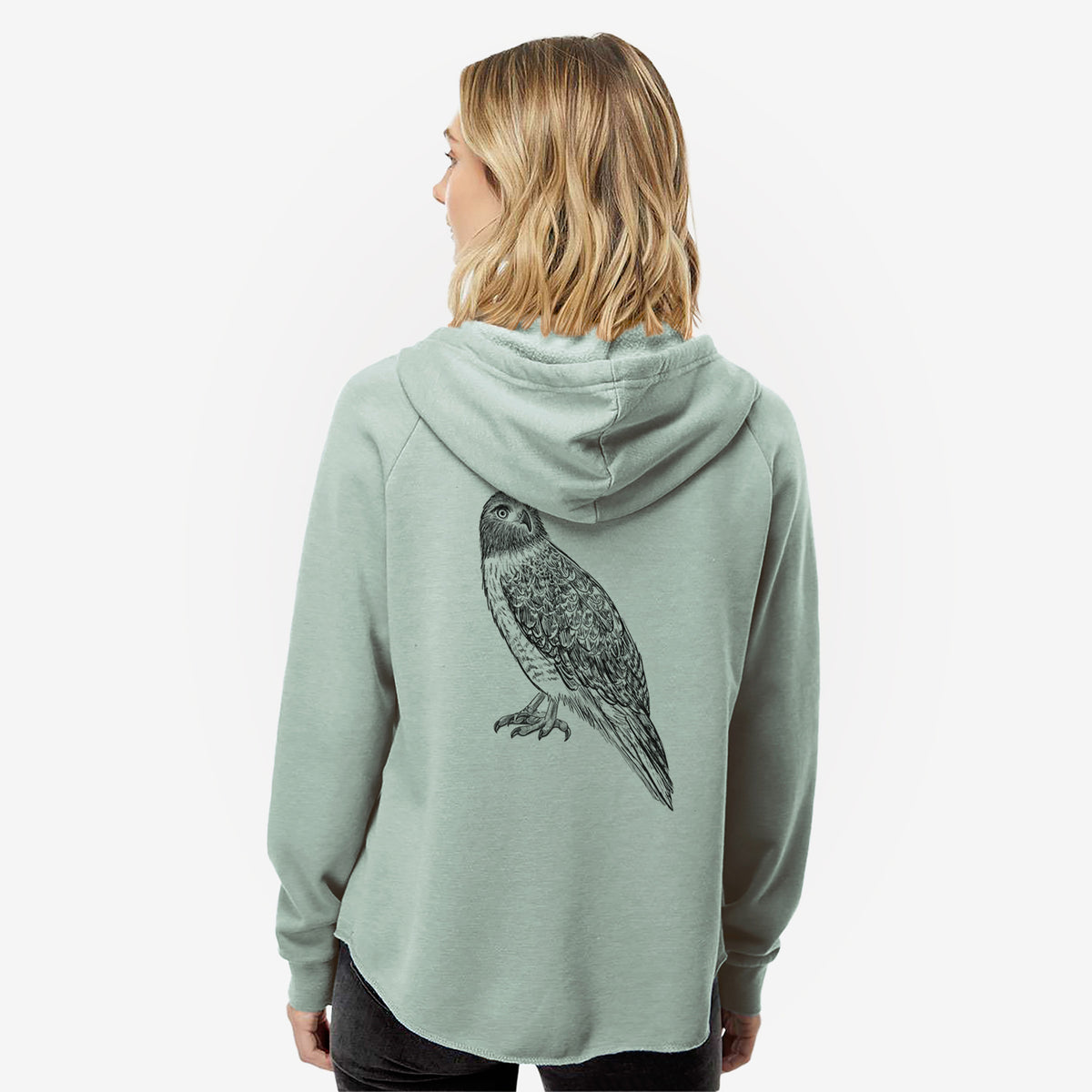 Woman wearing a sage green women's Cali Wave zip-up sweatshirt printed with a detailed black ink illustration of a red-tailed hawk perched, seen from behind.