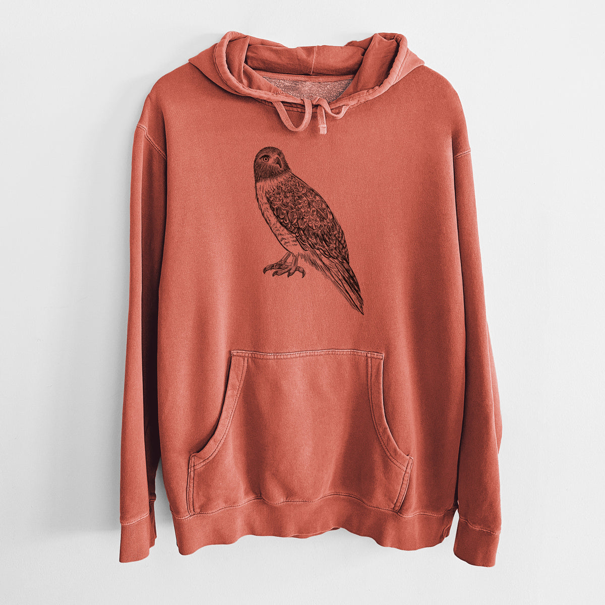 Amber orange pigment dyed hoodie laid flat, printed with a detailed black ink illustration of a red-tailed hawk perched.