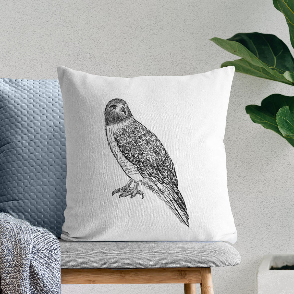 White pillow cover printed with a detailed black ink illustration of a red-tailed hawk perched, on a bench beside plants.