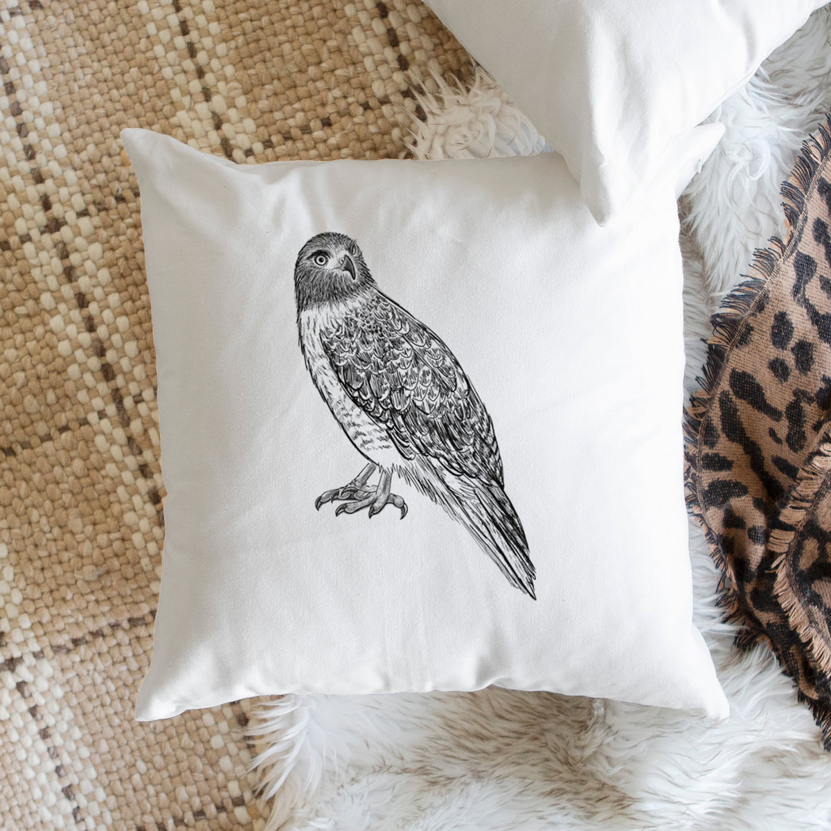 White pillow cover printed with a detailed black ink illustration of a red-tailed hawk perched, on a woven chair.