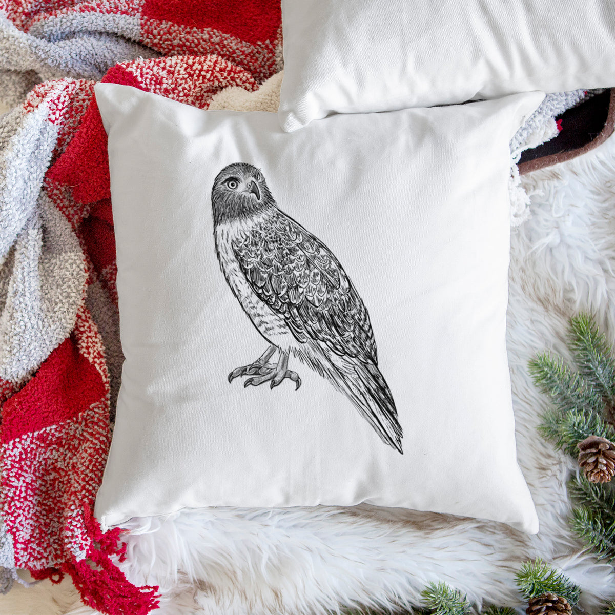 White pillow cover printed with a detailed black ink illustration of a red-tailed hawk perched, on a woven chair.