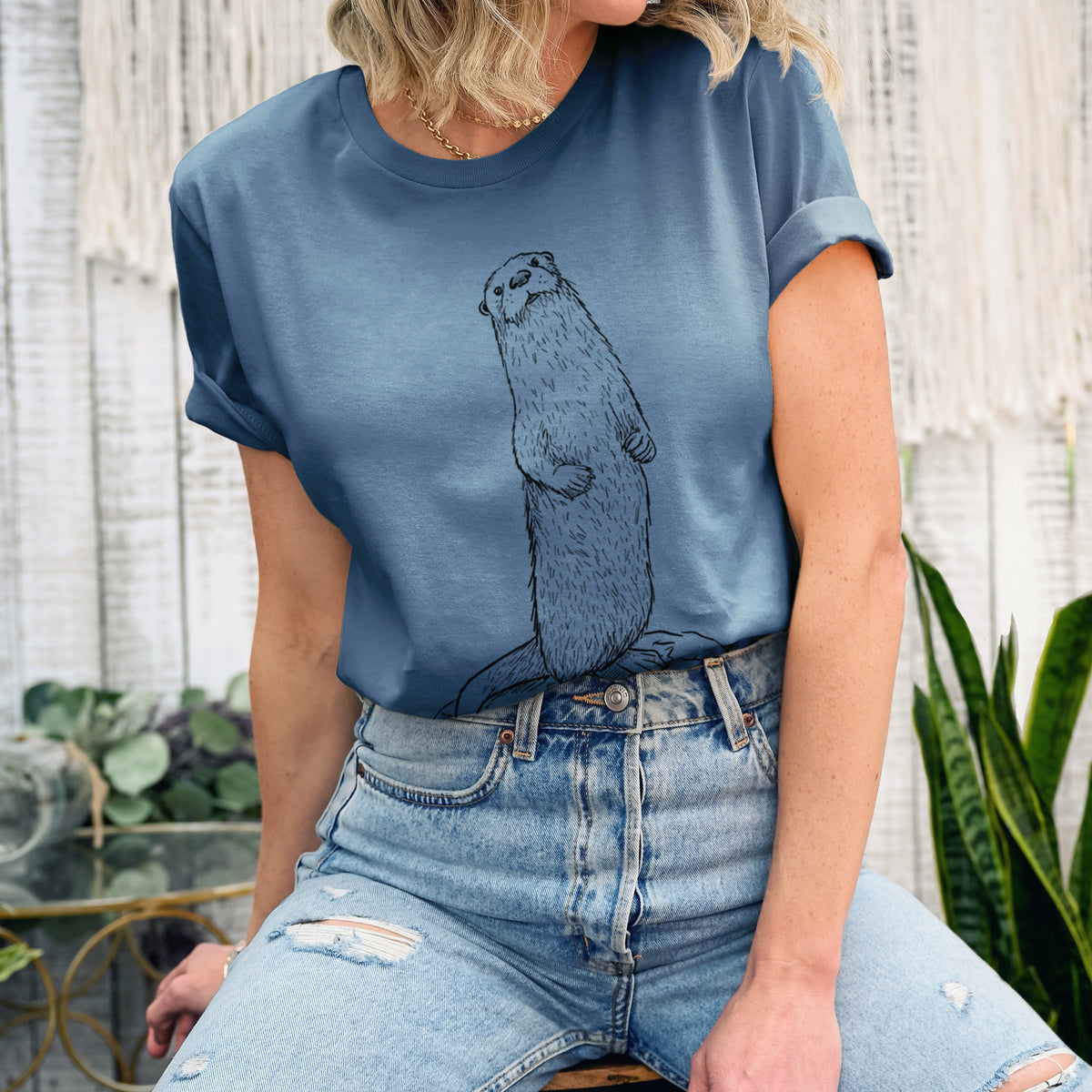Woman wearing a steel blue lightweight cotton t-shirt printed with a black ink illustration of a river otter standing upright on a rock.