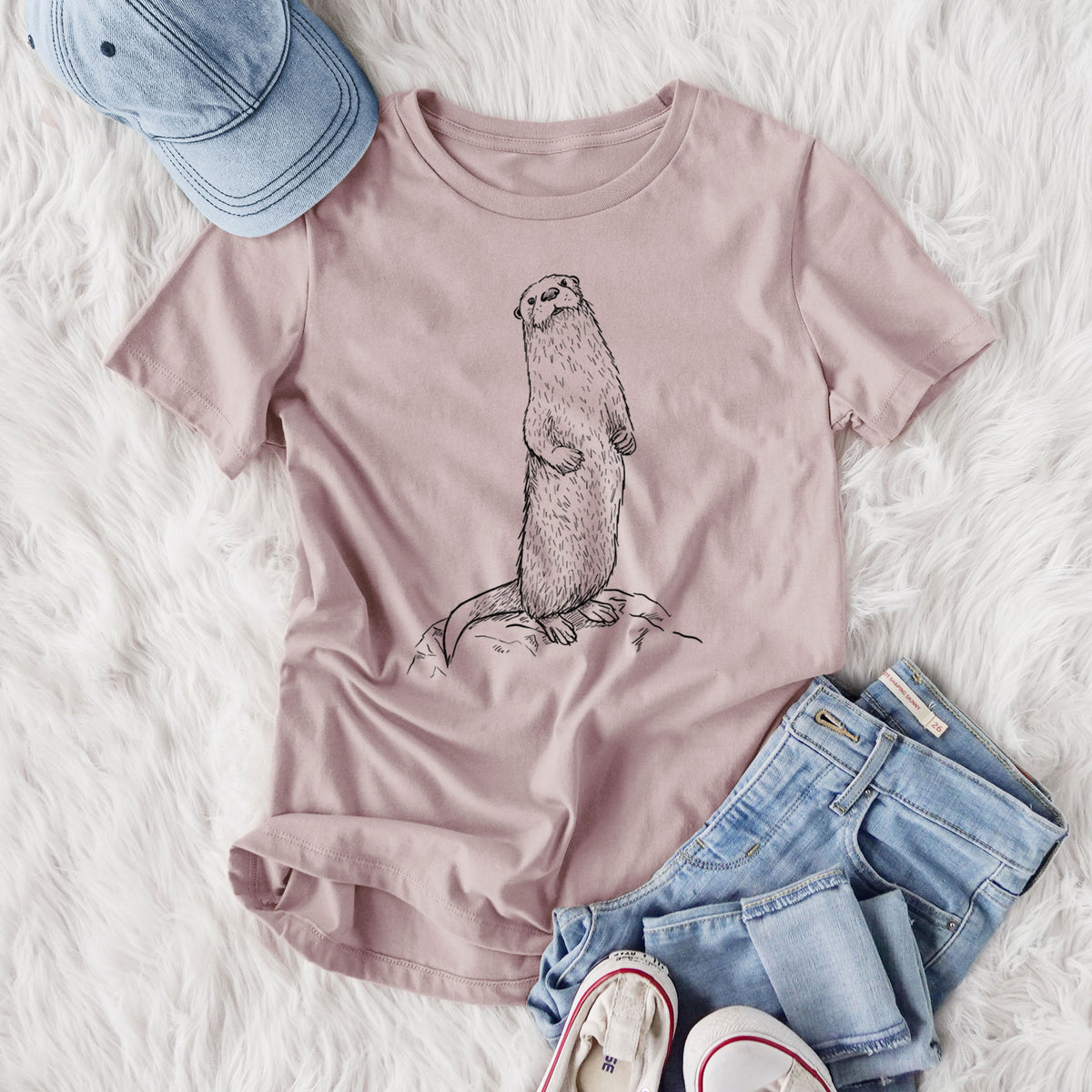 Women's relaxed fit cotton t-shirt printed with a black ink illustration of a river otter standing upright on a rock, styled flat on a white faux fur rug with jeans.