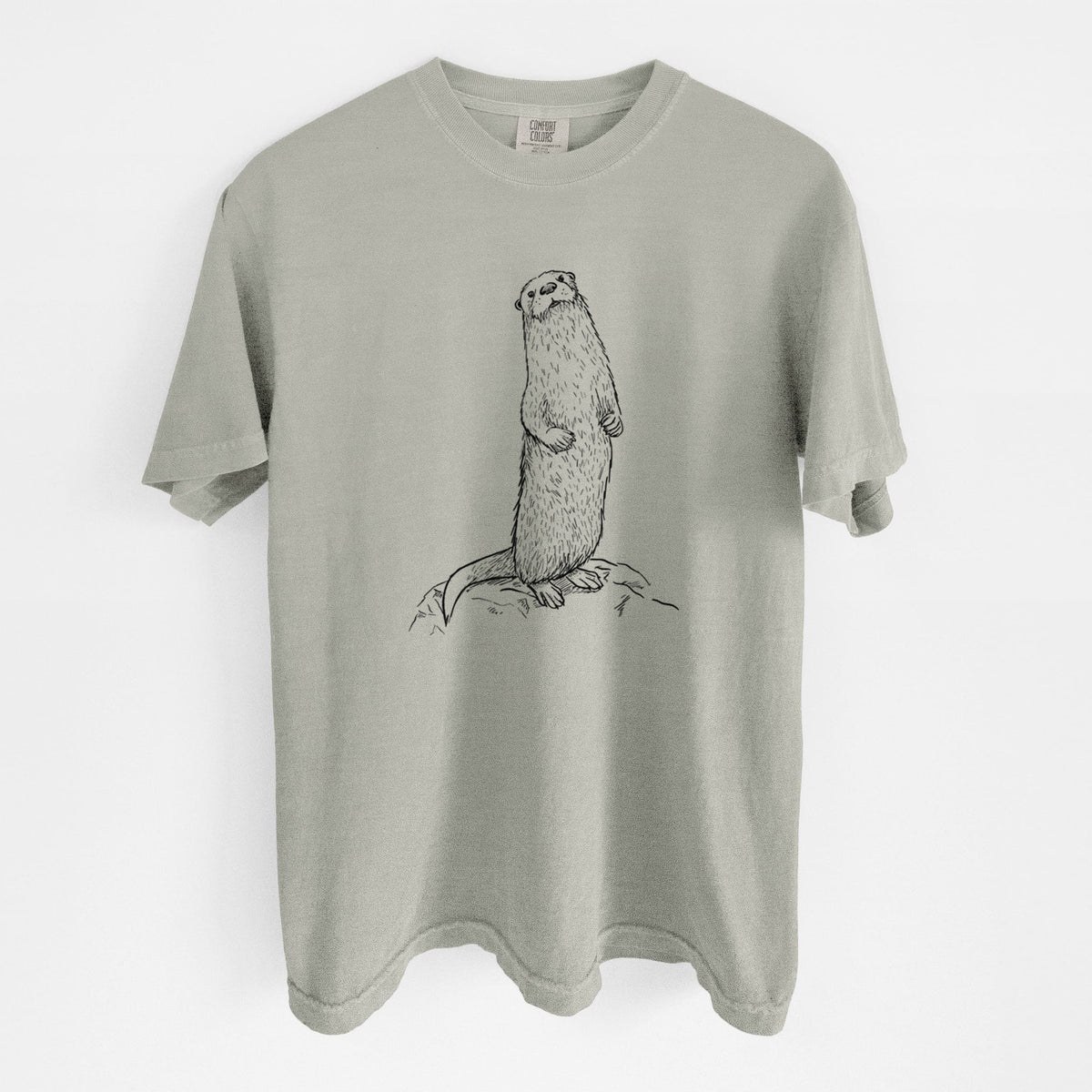 Sandstone beige Comfort Colors t-shirt laid flat, printed with a black ink illustration of a river otter standing upright on a rock.